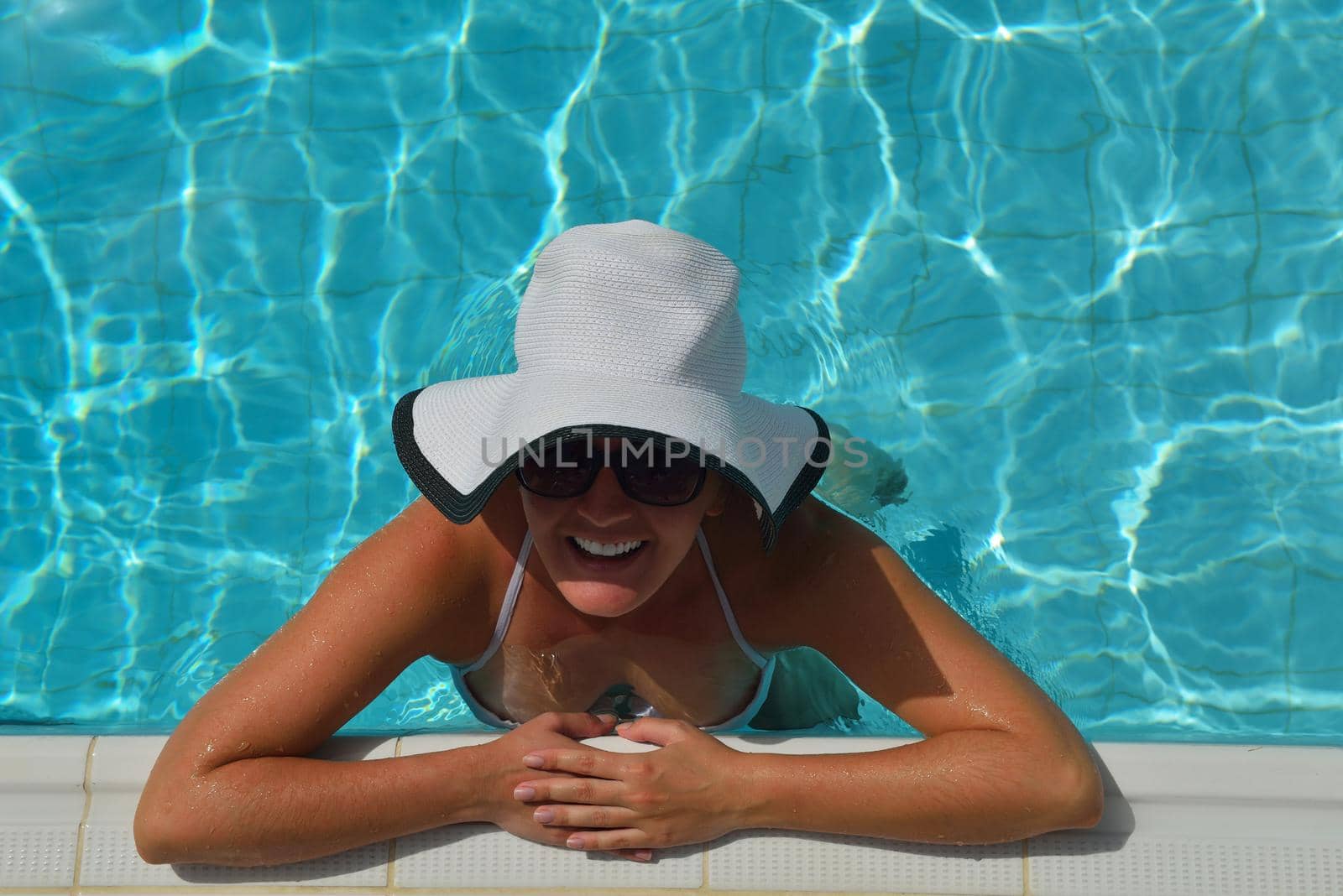 Happy smiling woman with hat and sunglasses  in swimming pool at tropical resort