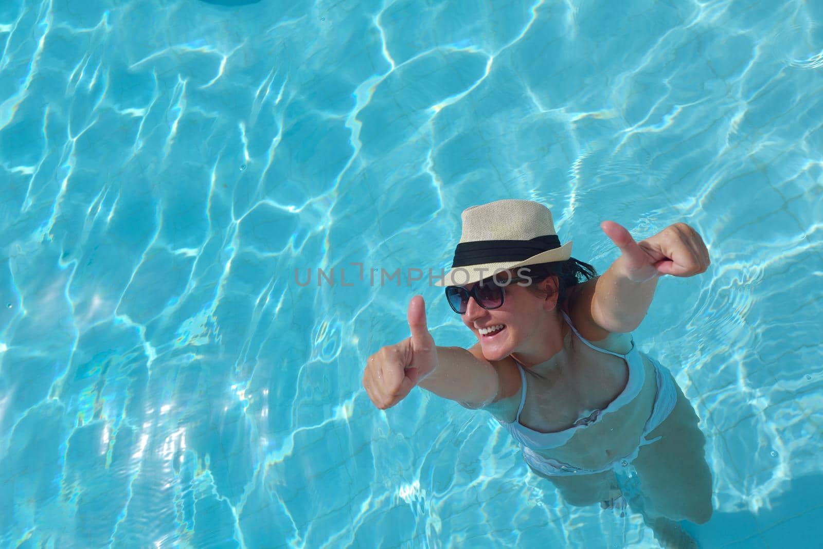 Happy smiling woman with hat and sunglasses  in swimming pool at tropical resort