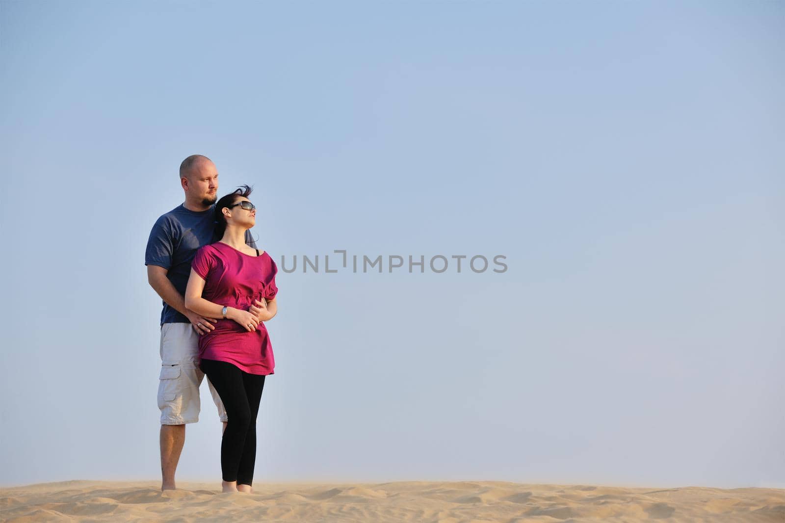 relaxed young pasionate couple enjoying the sunset  beauty on their honeymoon, on a desert with orange background