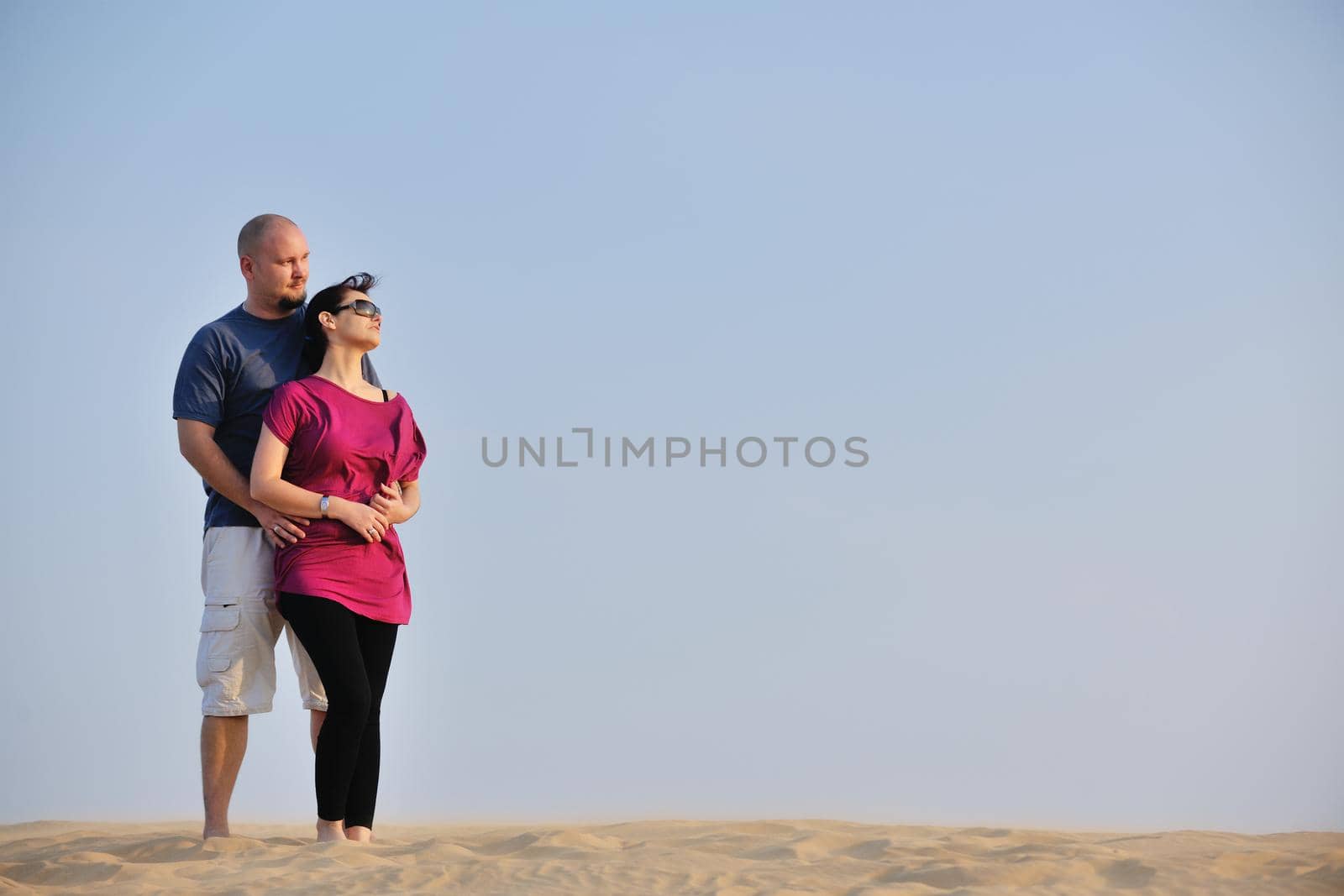 relaxed young pasionate couple enjoying the sunset  beauty on their honeymoon, on a desert with orange background