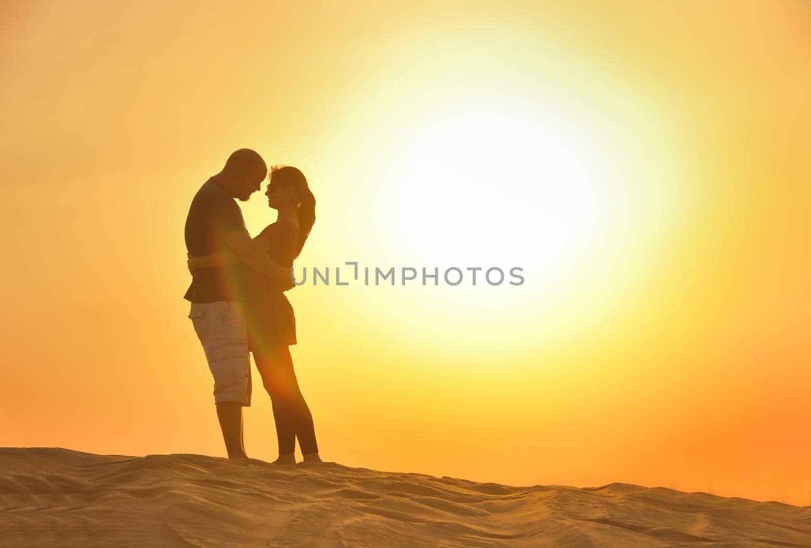 relaxed young pasionate couple enjoying the sunset  beauty on their honeymoon, on a desert with orange background