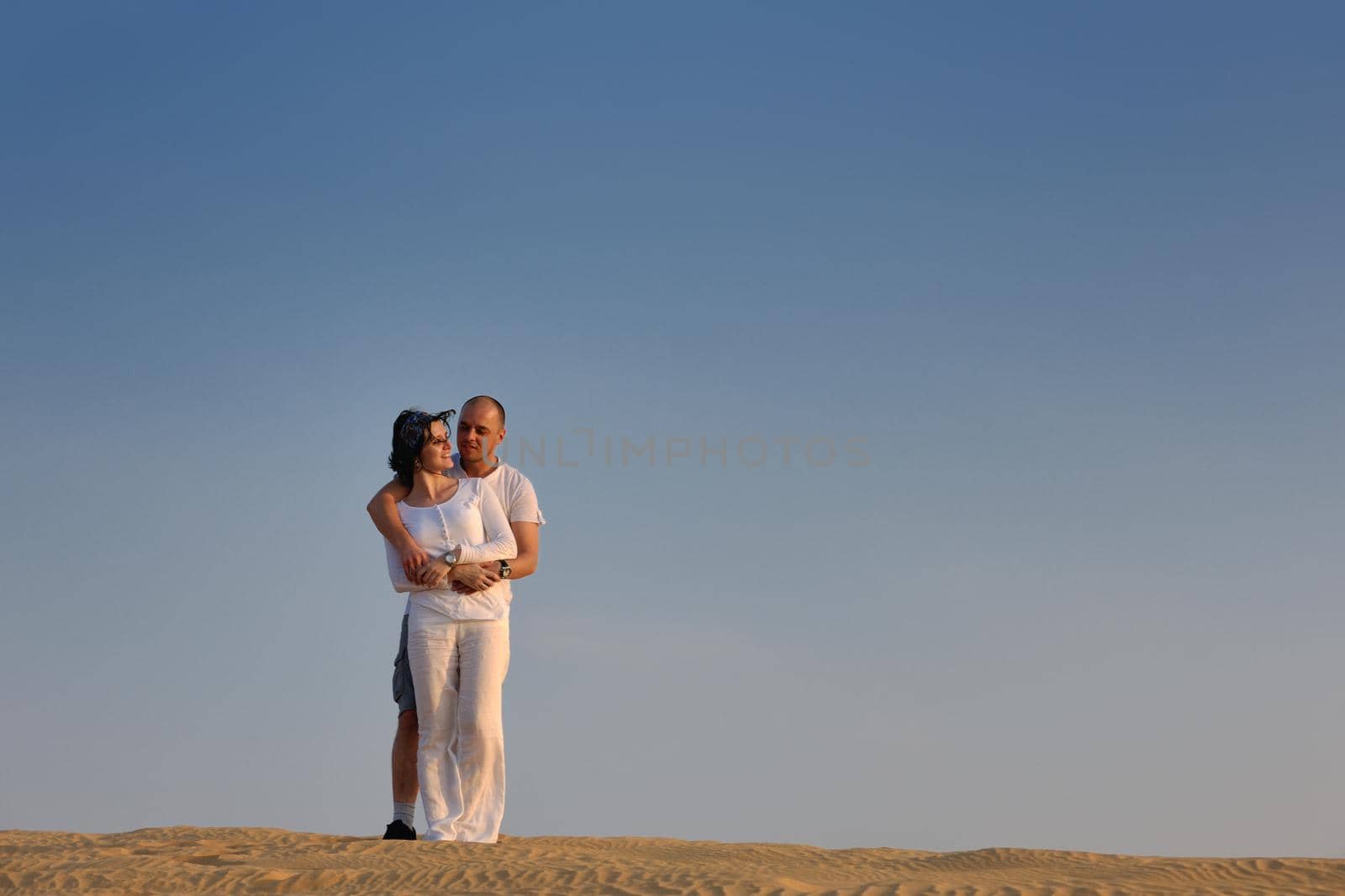 relaxed young pasionate couple enjoying the sunset  beauty on their honeymoon, on a desert with orange background