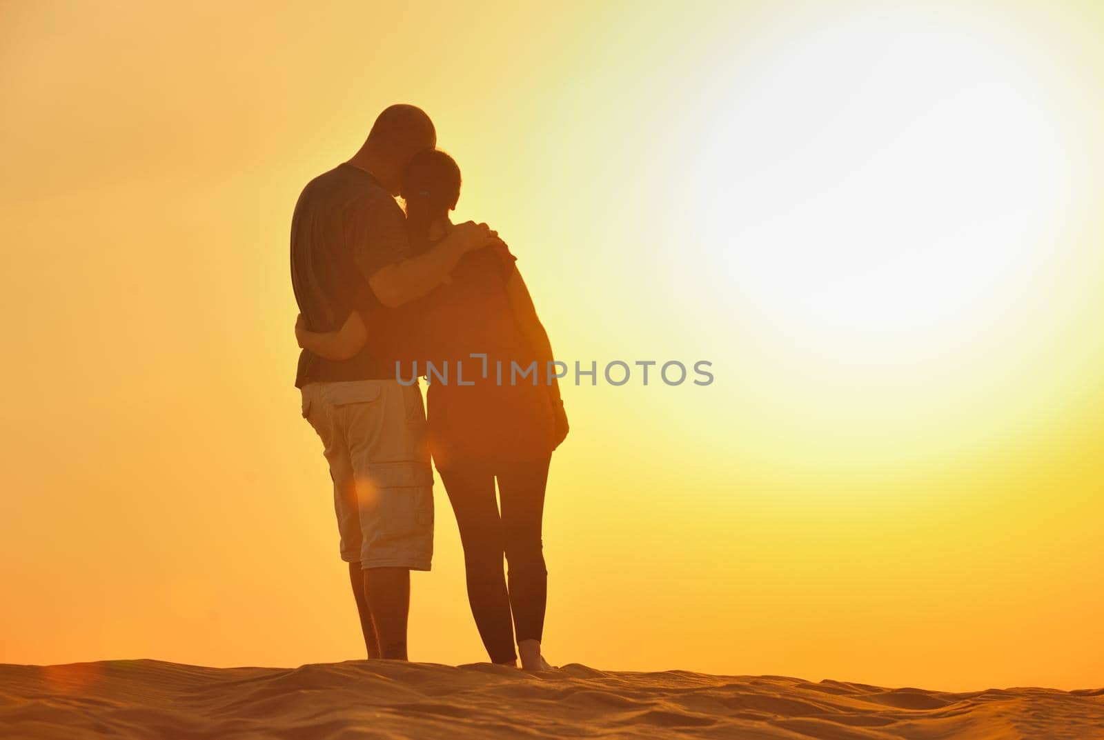 relaxed young pasionate couple enjoying the sunset  beauty on their honeymoon, on a desert with orange background