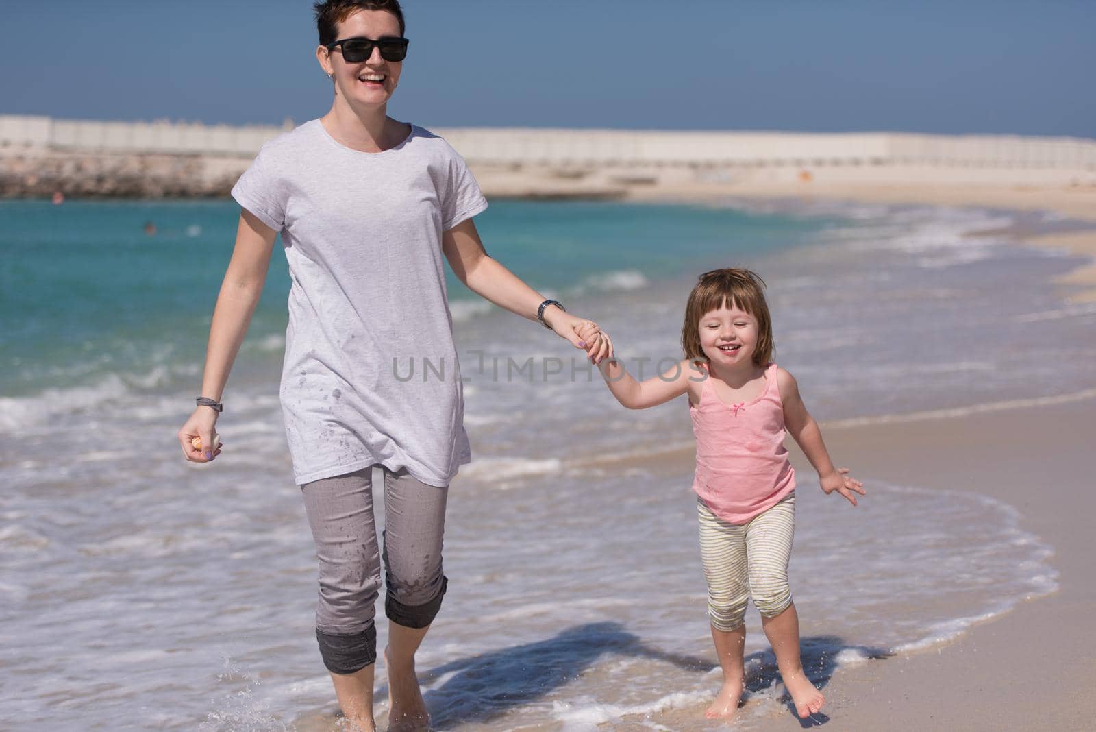 beautiful young mother and cute little girl are enjoying while running on exotic beach along the ocean Travel and Vacations.