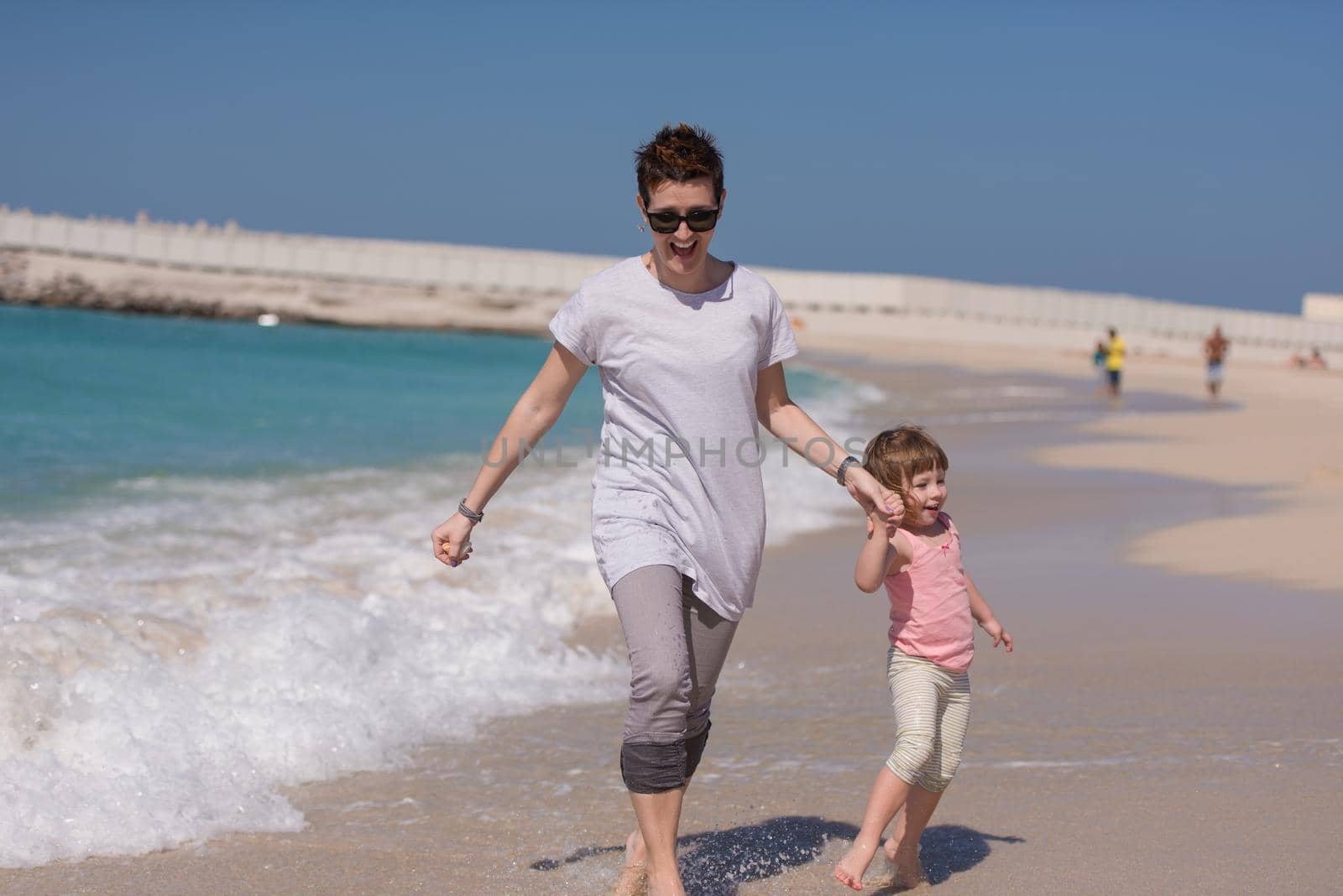 beautiful young mother and cute little girl are enjoying while running on exotic beach along the ocean Travel and Vacations.