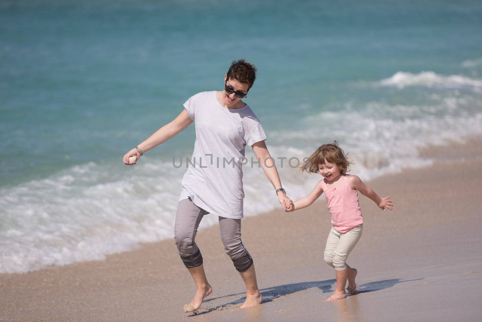 beautiful young mother and cute little girl are enjoying while running on exotic beach along the ocean Travel and Vacations.