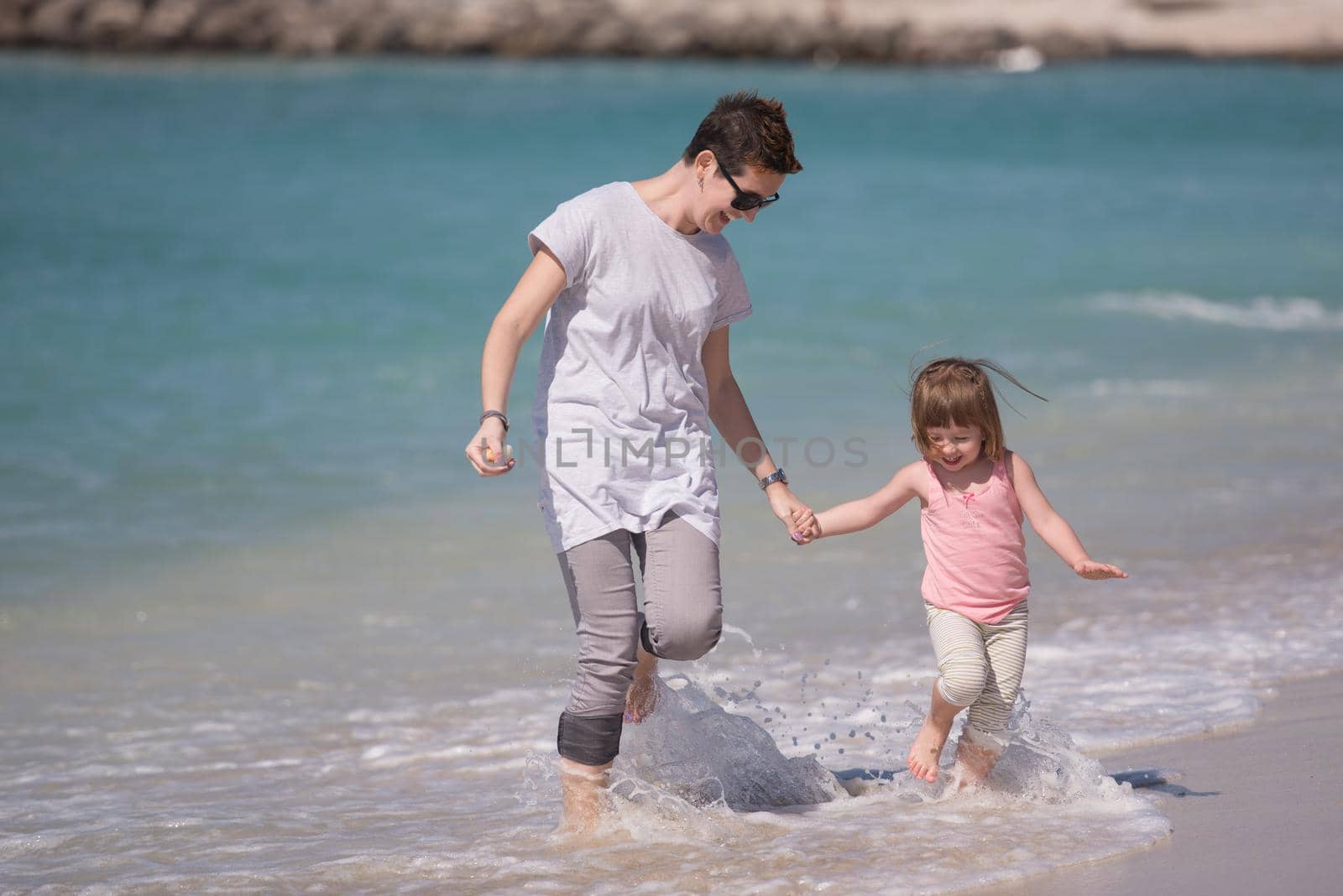 beautiful young mother and cute little girl are enjoying while running on exotic beach along the ocean Travel and Vacations.