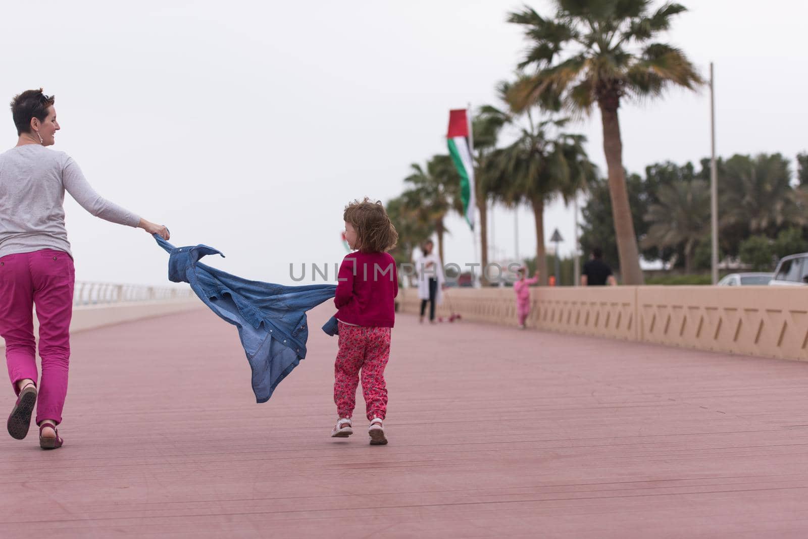 young mother and cute little girl running and cheerfully spend their time on the promenade by the sea