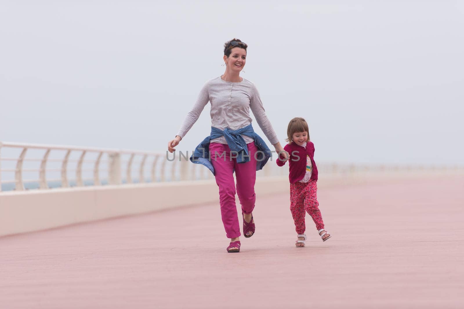 young mother and cute little girl running and cheerfully spend their time on the promenade by the sea