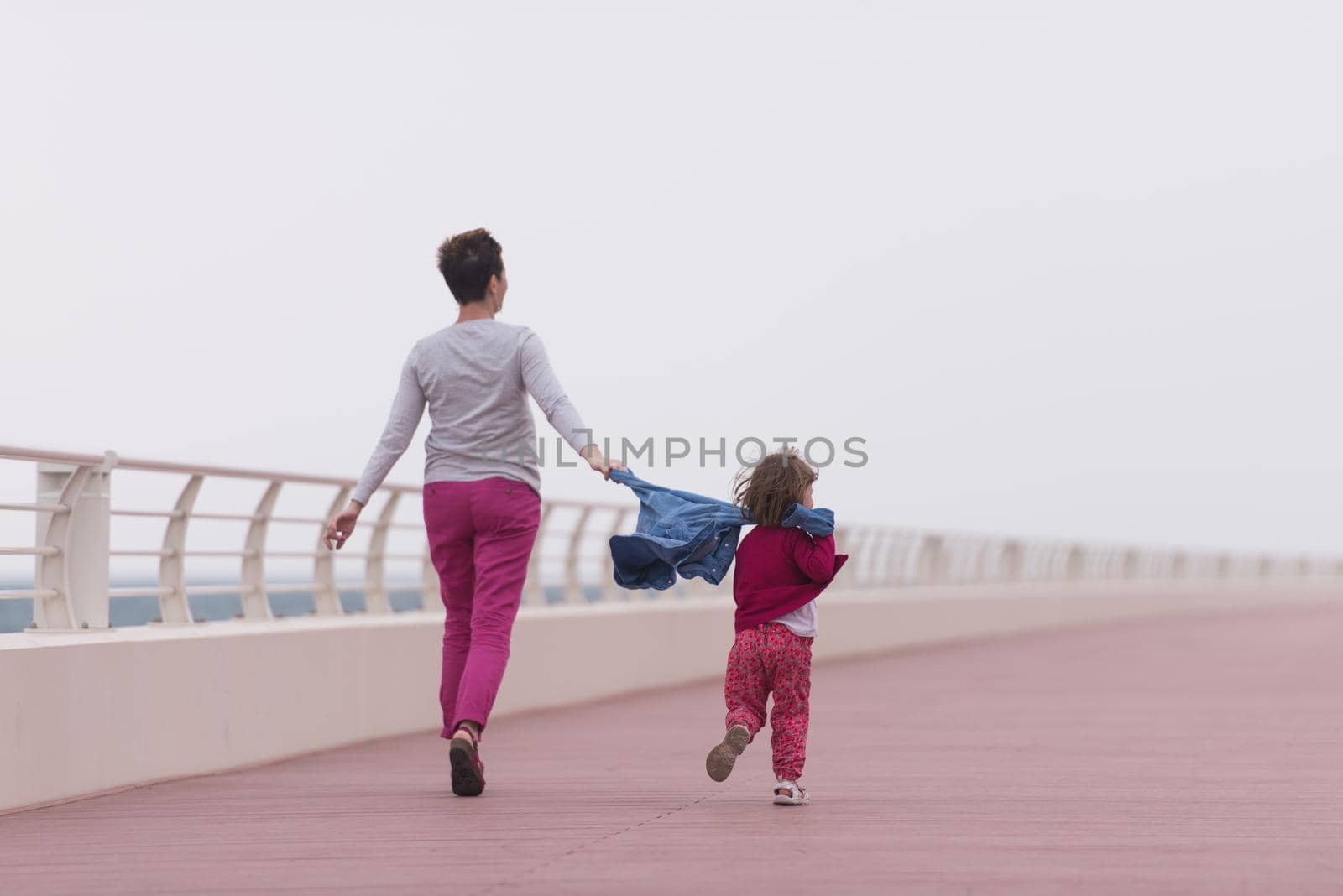 young mother and cute little girl running and cheerfully spend their time on the promenade by the sea