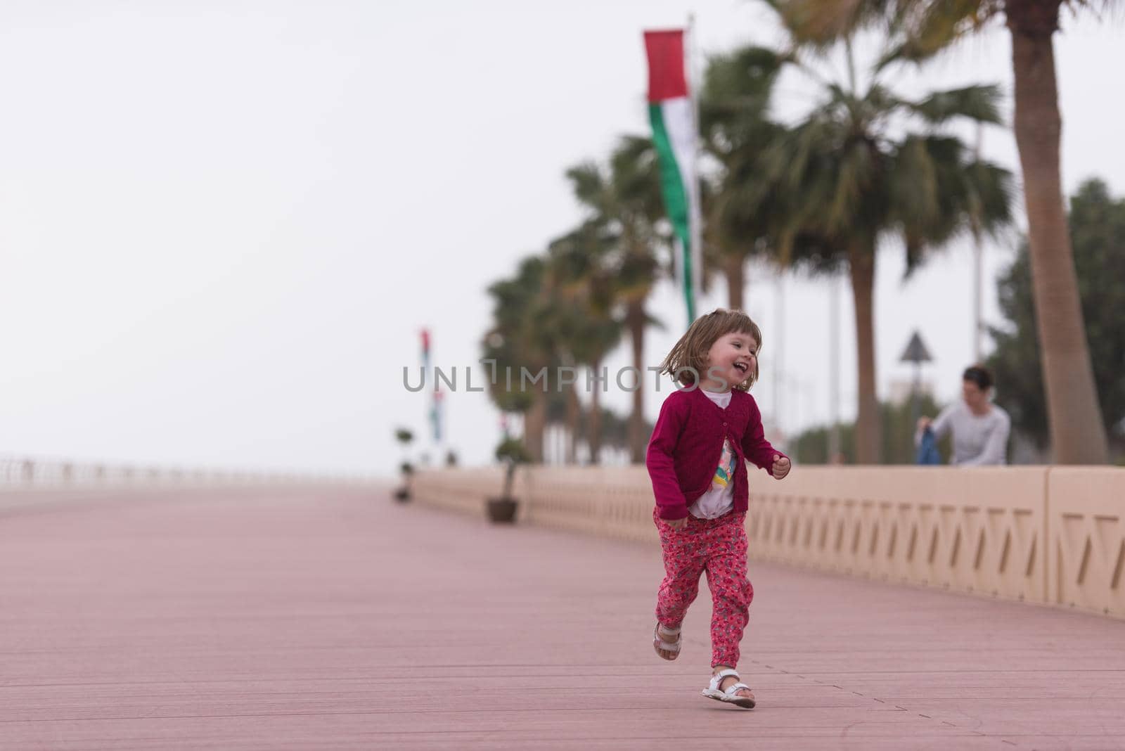 young mother and cute little girl running and cheerfully spend their time on the promenade by the sea