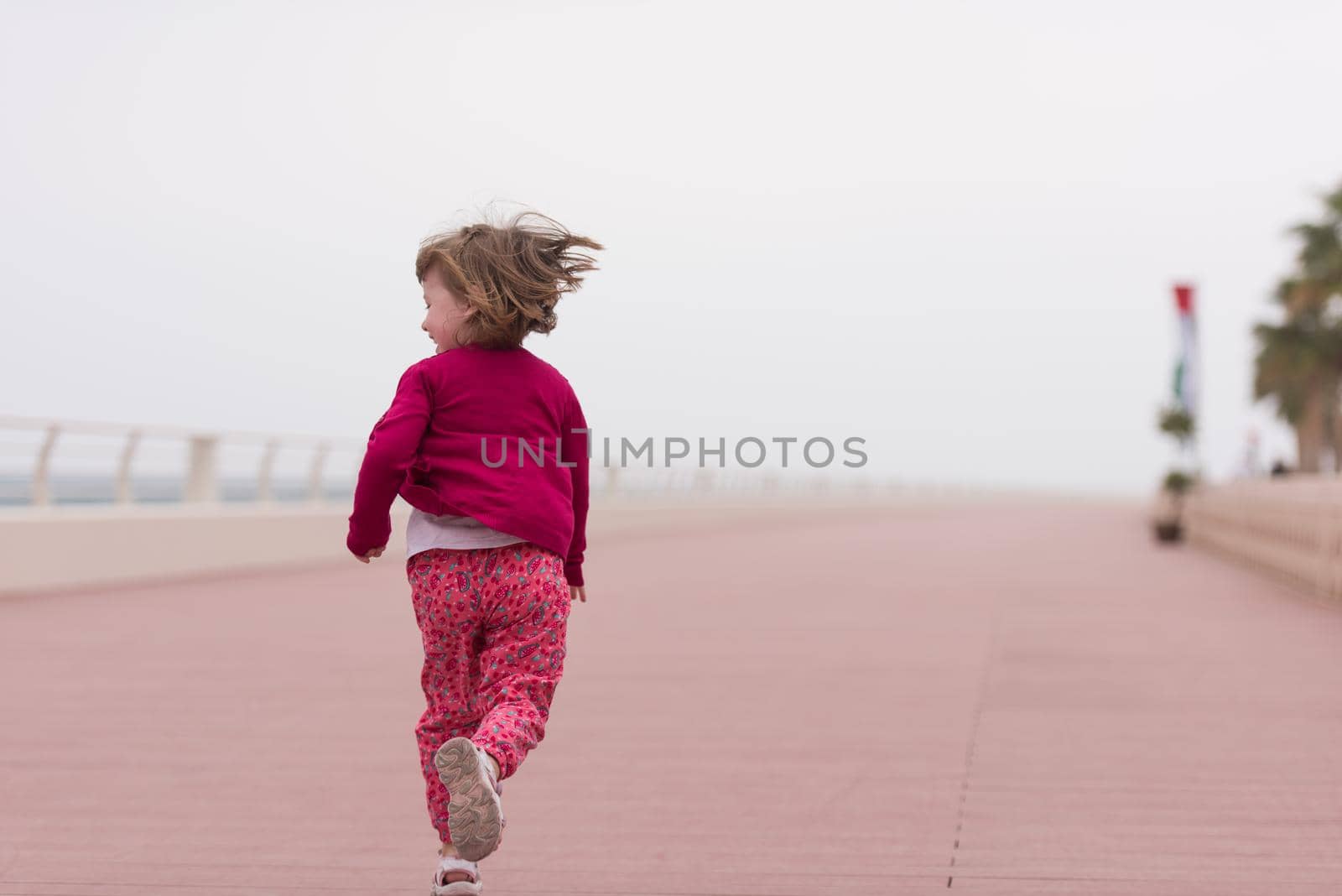 cute little girl running and cheerfully spend her time on the promenade by the sea