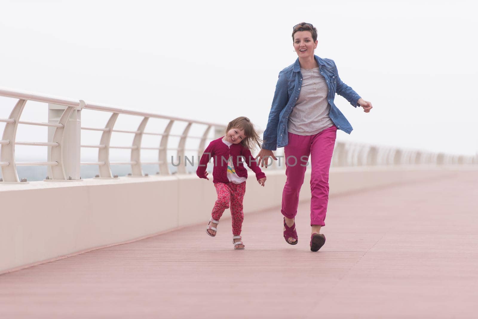 young mother and cute little girl running and cheerfully spend their time on the promenade by the sea