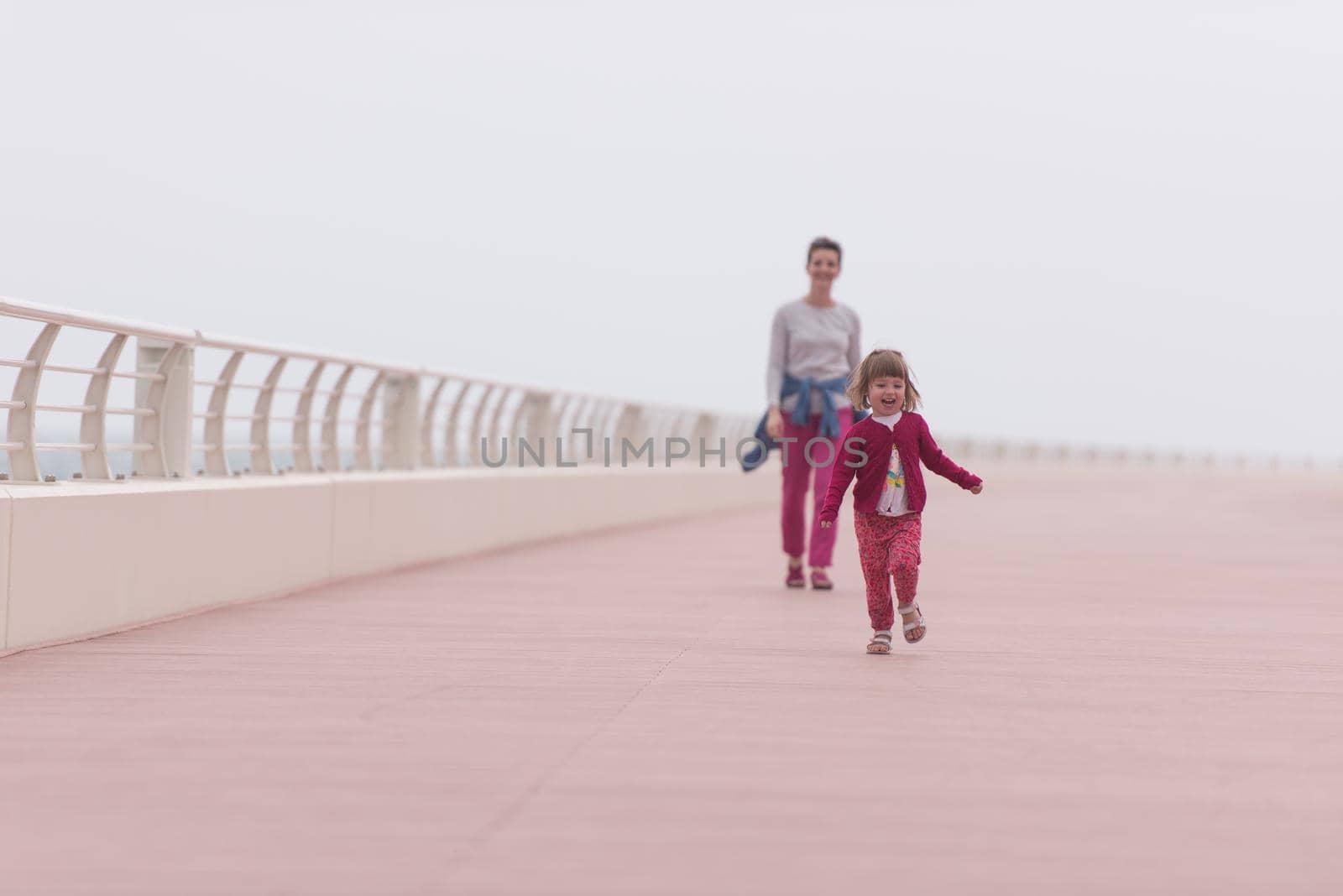 young mother and cute little girl running and cheerfully spend their time on the promenade by the sea