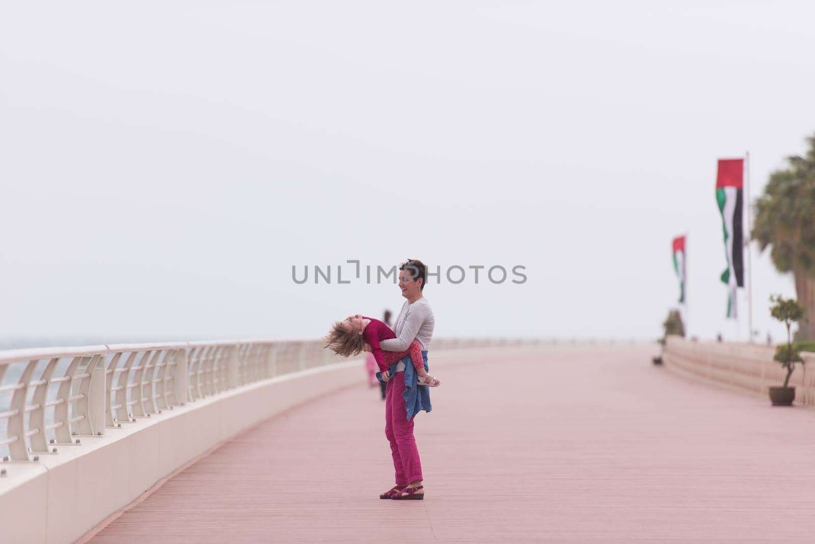 young mother and cute little girl running and cheerfully spend their time on the promenade by the sea