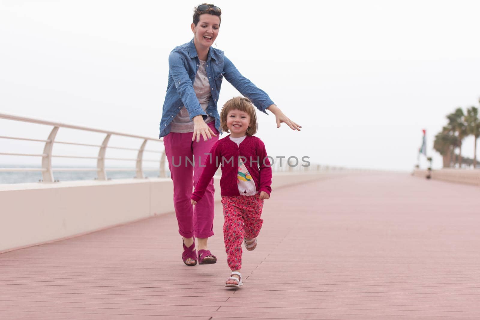 young mother and cute little girl running and cheerfully spend their time on the promenade by the sea