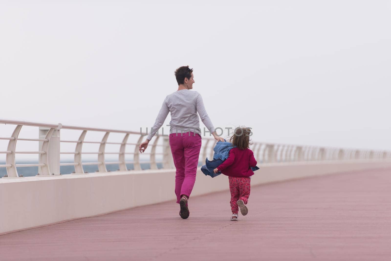 young mother and cute little girl running and cheerfully spend their time on the promenade by the sea