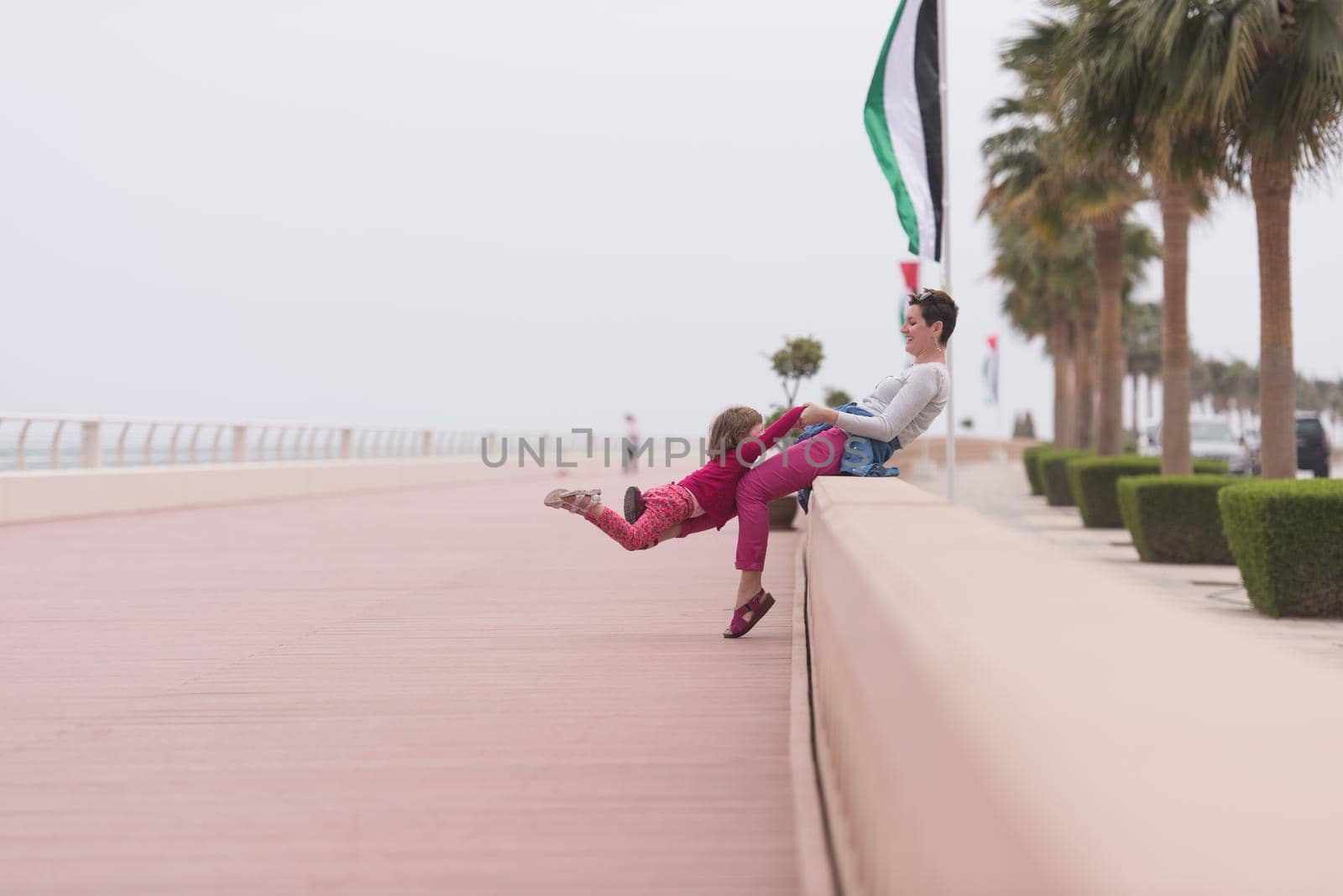 young mother and cute little girl running and cheerfully spend their time on the promenade by the sea