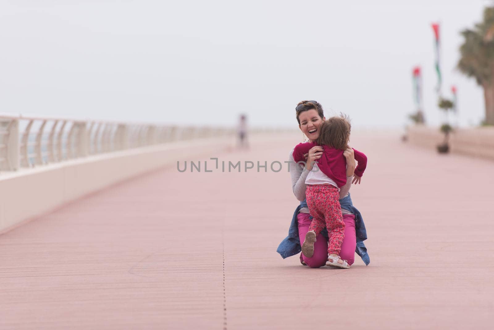 young mother and cute little girl running and cheerfully spend their time on the promenade by the sea