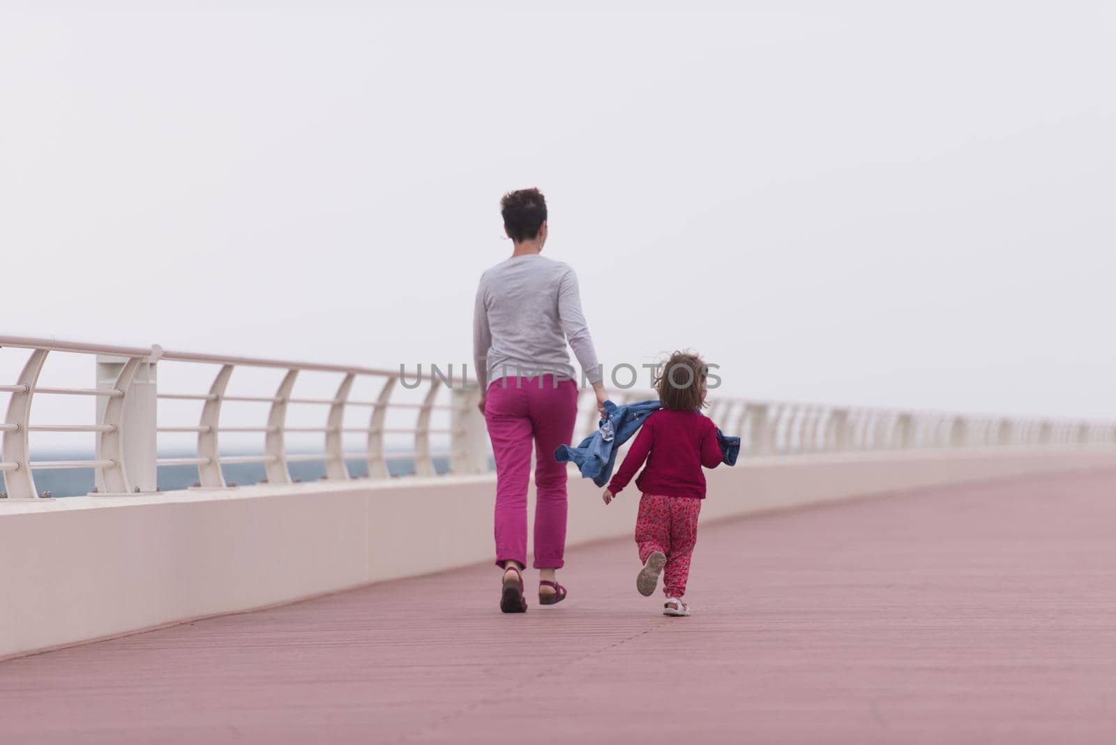 young mother and cute little girl running and cheerfully spend their time on the promenade by the sea