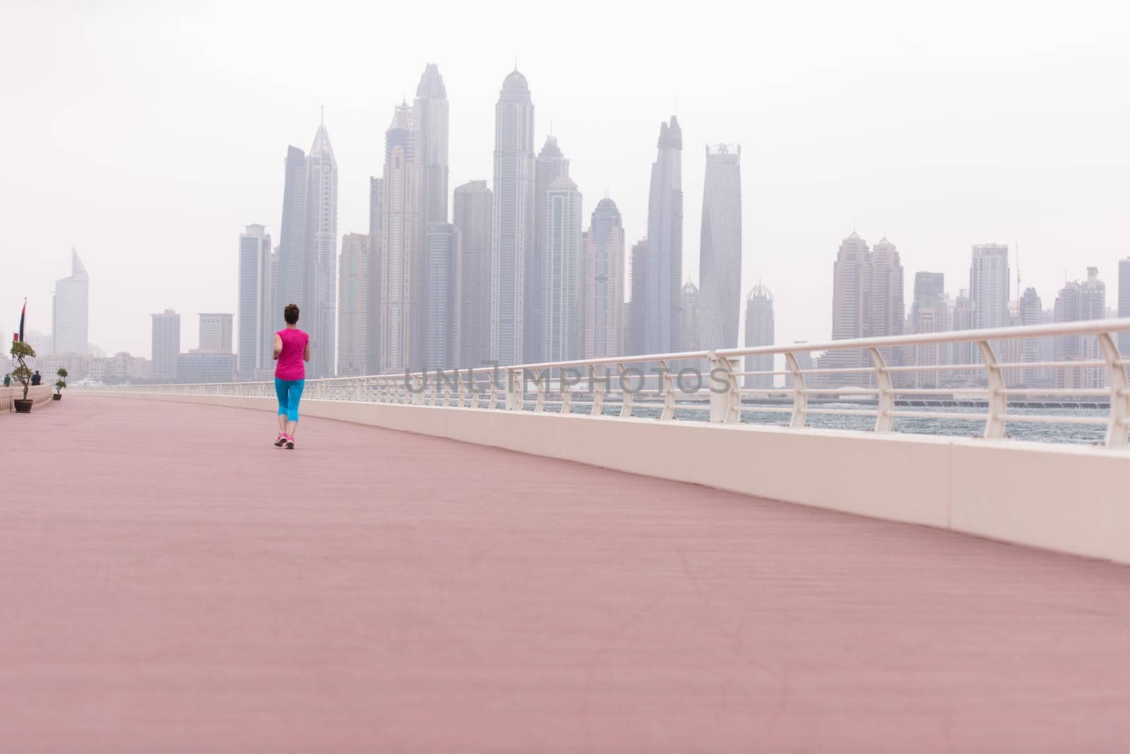 very active young beautiful woman busy running on the promenade along the ocean side with a big modern city in the background to keep up her fitness levels as much as possible