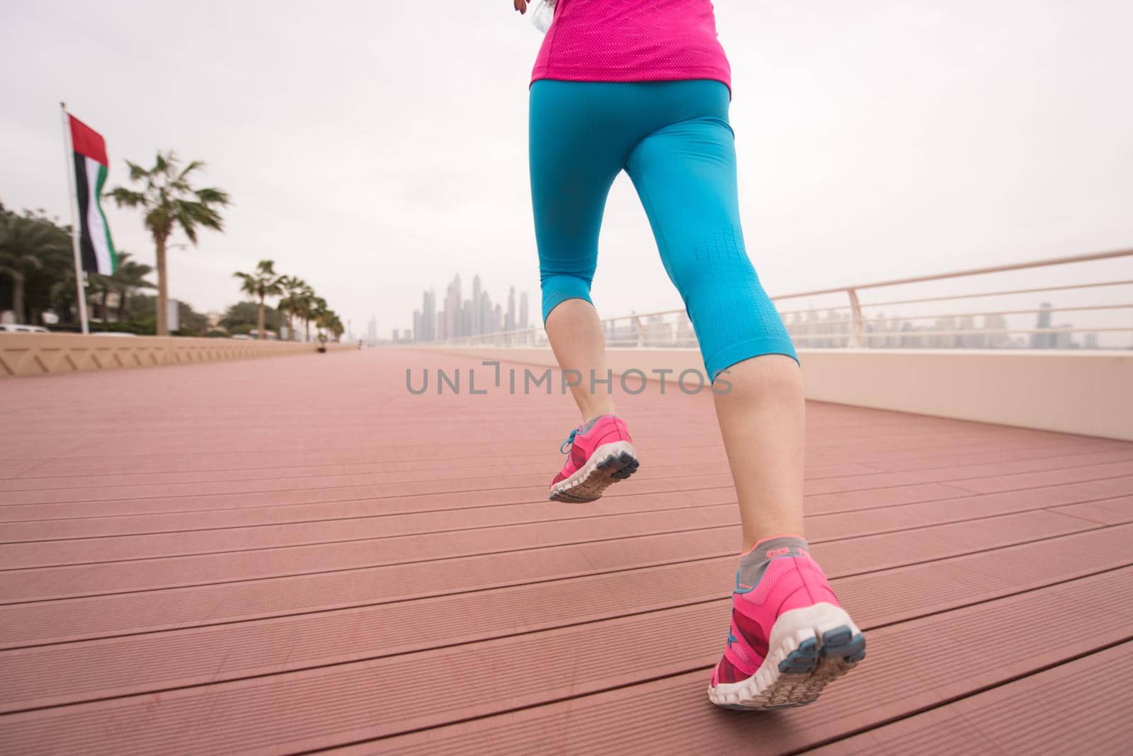 very active young beautiful woman busy running on the promenade along the ocean side with a big modern city in the background to keep up her fitness levels as much as possible