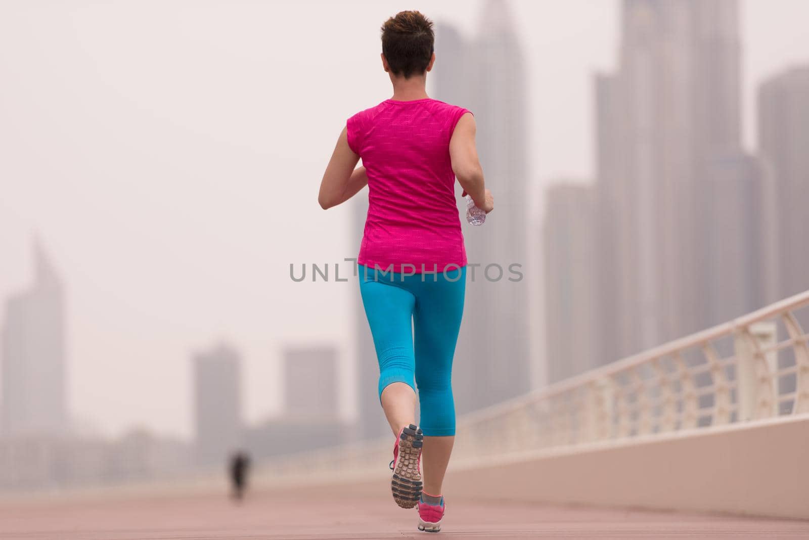 very active young beautiful woman busy running on the promenade along the ocean side with a big modern city in the background to keep up her fitness levels as much as possible