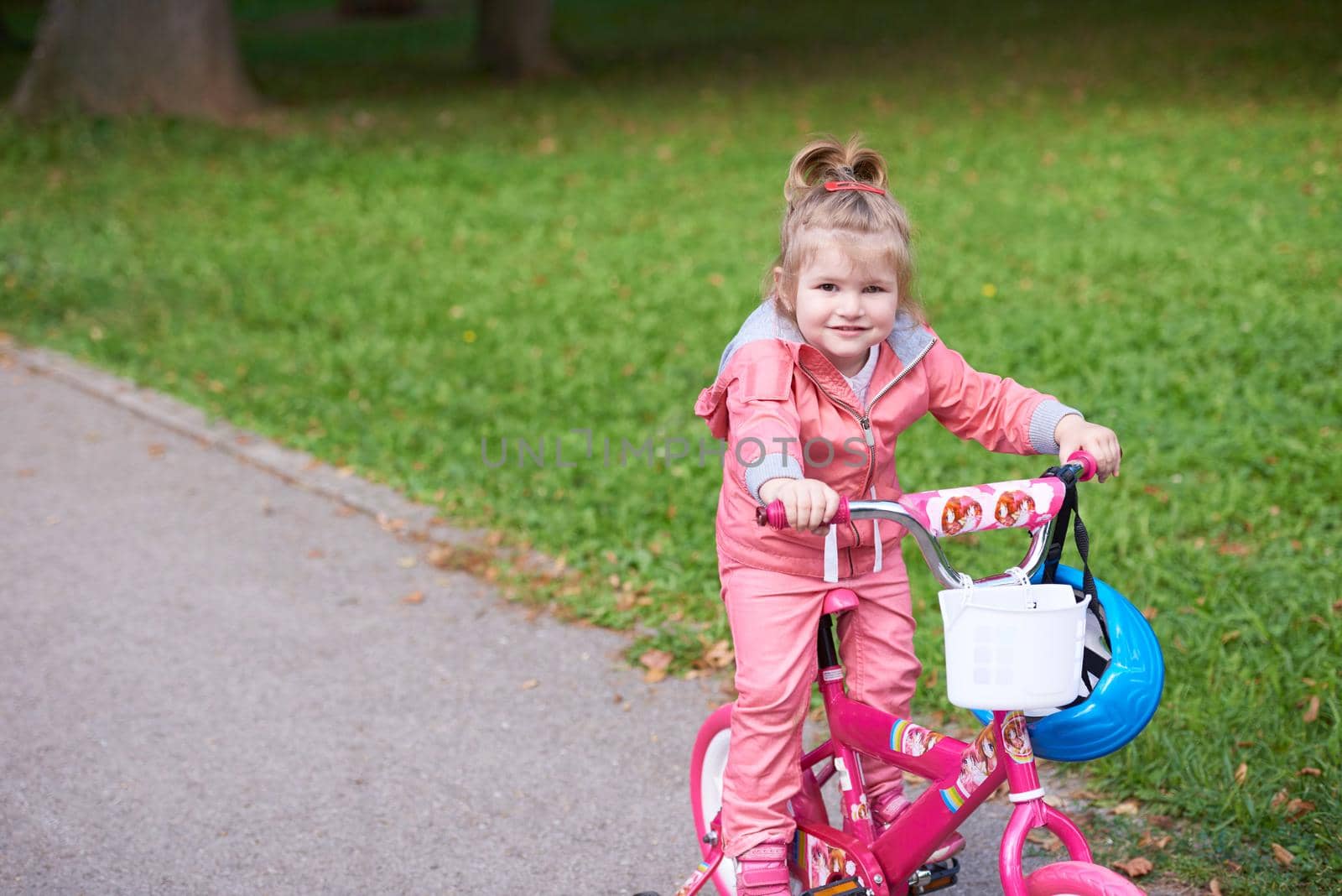 Cute smiling little girl with bicycle and helmet on road in the park