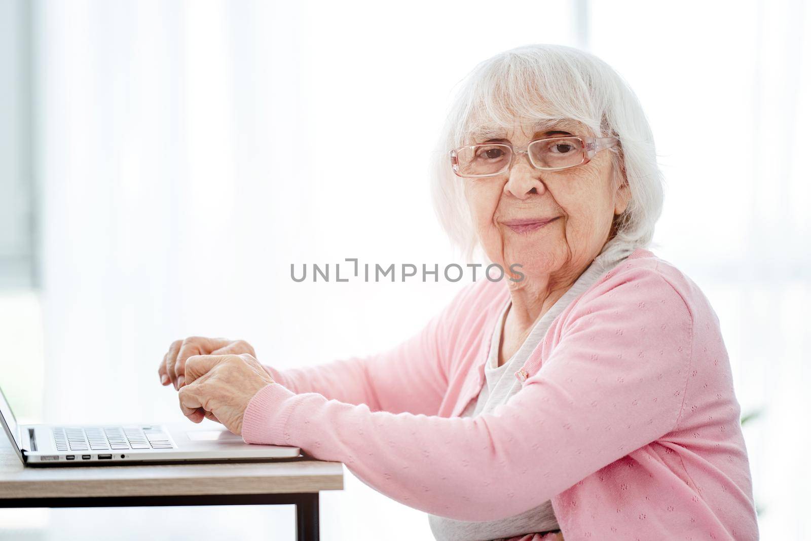 Senior woman using laptop at home and looking at the camera. Elderly person with modern technologies portrait