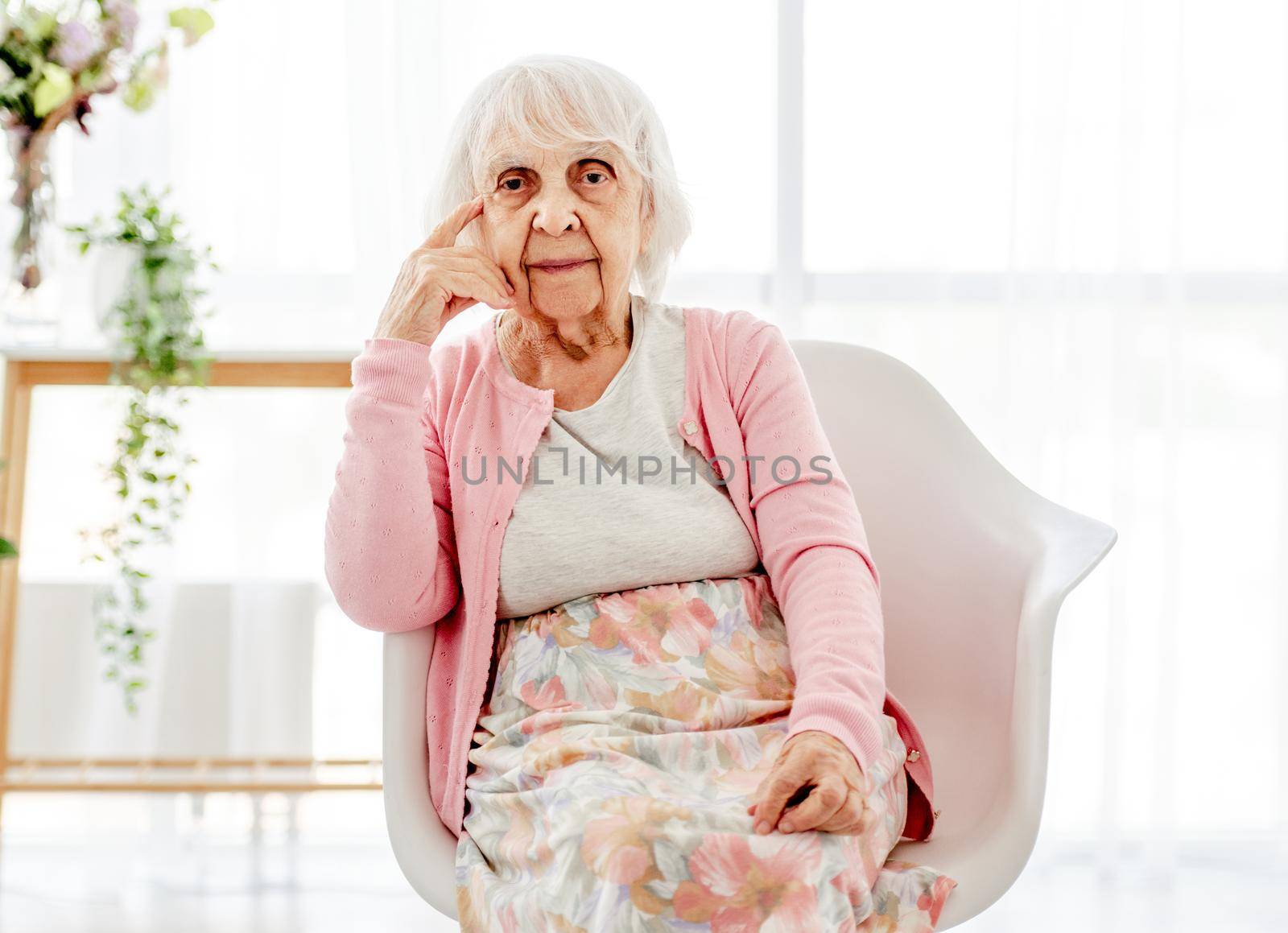Senior woman sitting and looking at the camera. Pensioner elderly person portrait at home