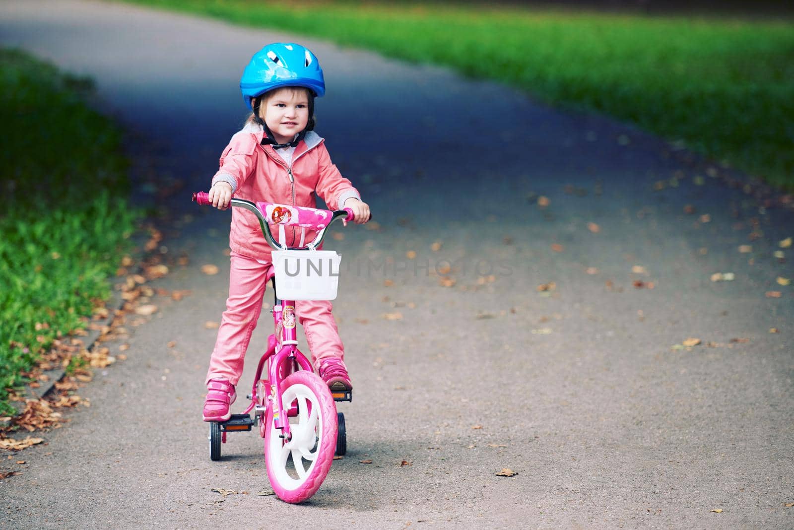 Cute smiling little girl with bicycle and helmet on road in the park