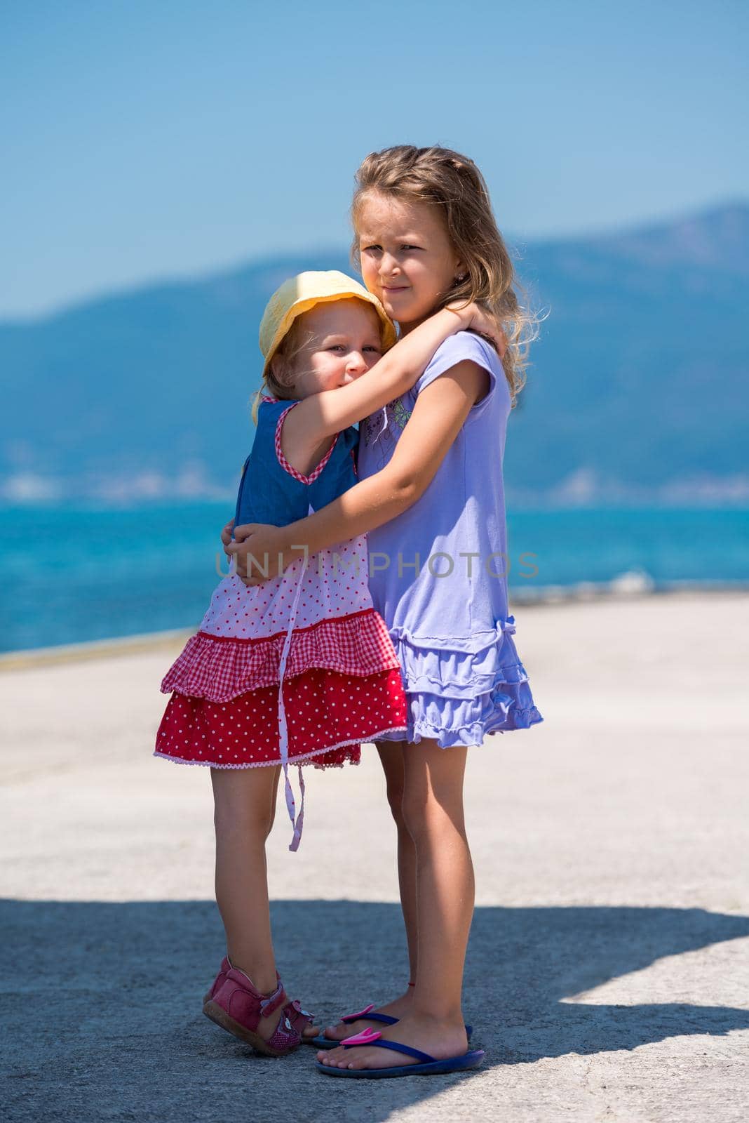 Happy smiling little sisters having fun while hugging on the beach coast during Summer vacation  Healthy childhood lifestyle concept