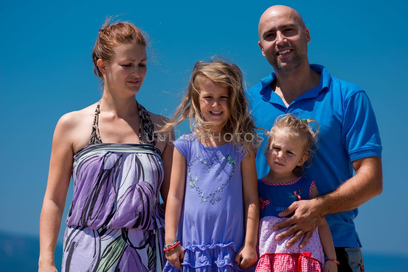 portrait of young happy family with cute little daughters having fun on a bench by the sea during Summer vacation  Healthy family holiday concept