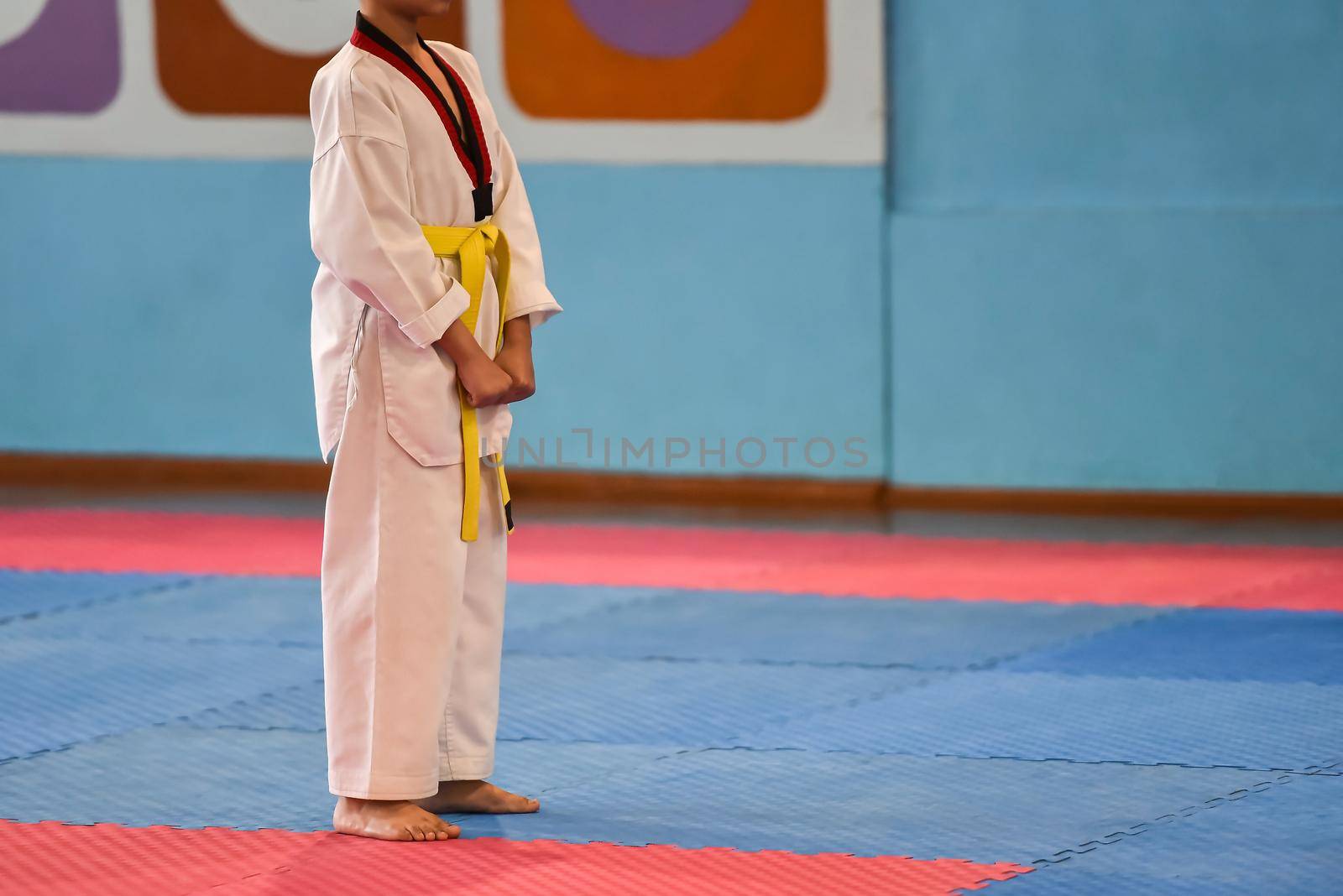 Taekwondo kids. A boy athlete stands in a taekwondo uniform with a yellow belt during a taekwondo tournament.