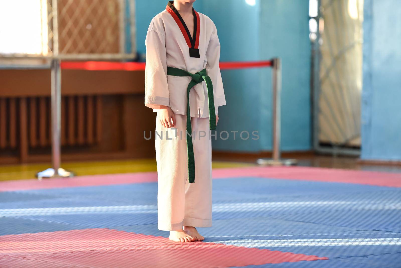 Taekwondo kids. A boy athlete stands in a taekwondo uniform with a green belt during a taekwondo tournament.