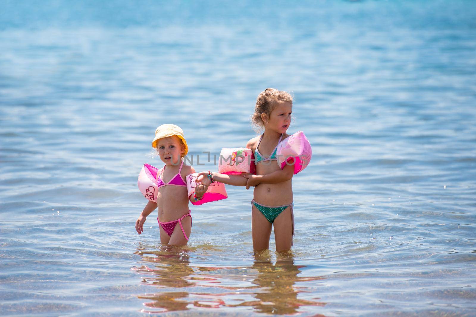 two happy little girls with swimming armbands playing in shallow water of the sea during Summer vacation  Healthy childhood lifestyle concept