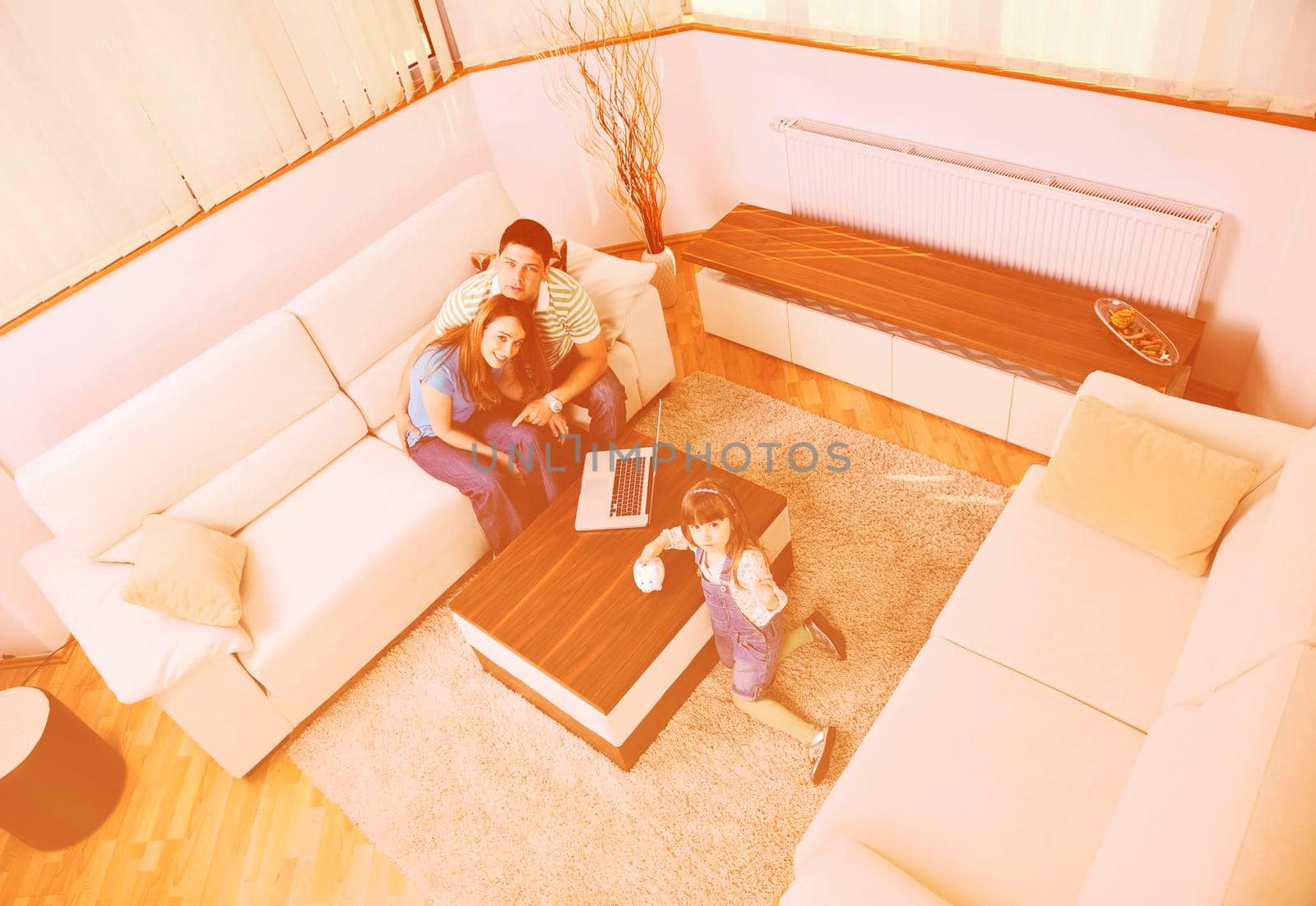 young happy family at bright and modern living room puting money in piggy bank and working on laptop computer on home finance