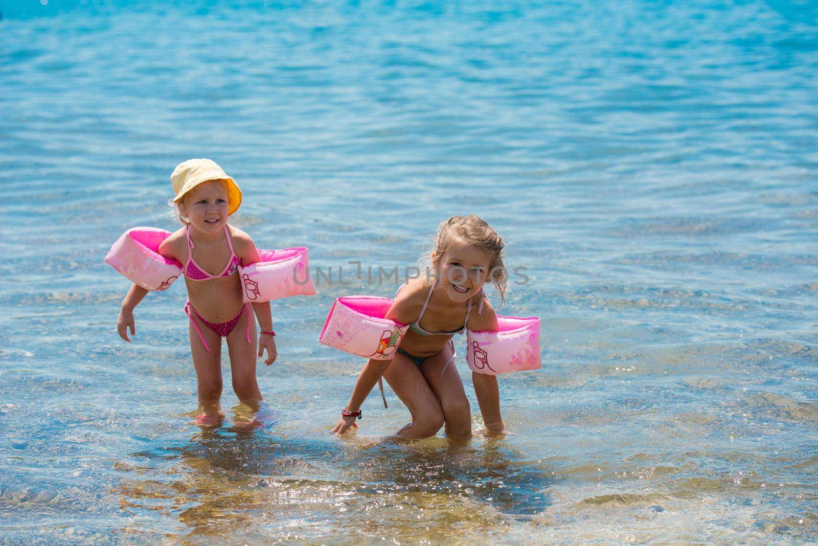 little girls with swimming armbands playing in shallow water by dotshock