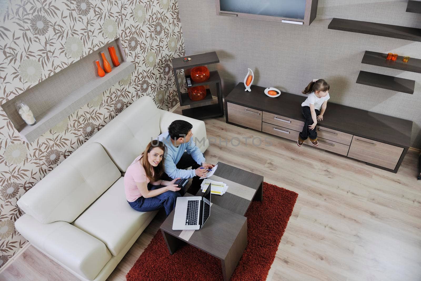 young happy family at bright and modern living room puting money in piggy bank and working on laptop computer on home finance