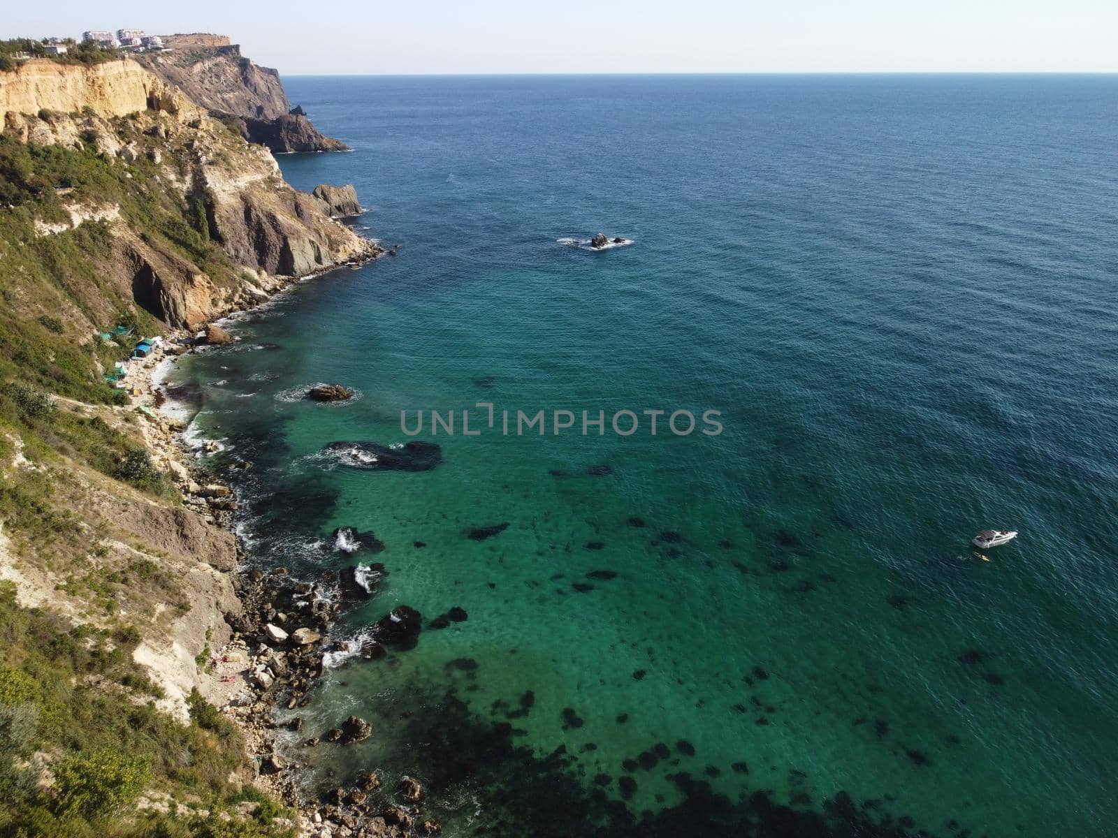 Sea landscape with rocky coastline on sunset time with cloudy sky. Yachts in the Sea on a background of rocky shores. The concept of perfect place for summer travel and rest.