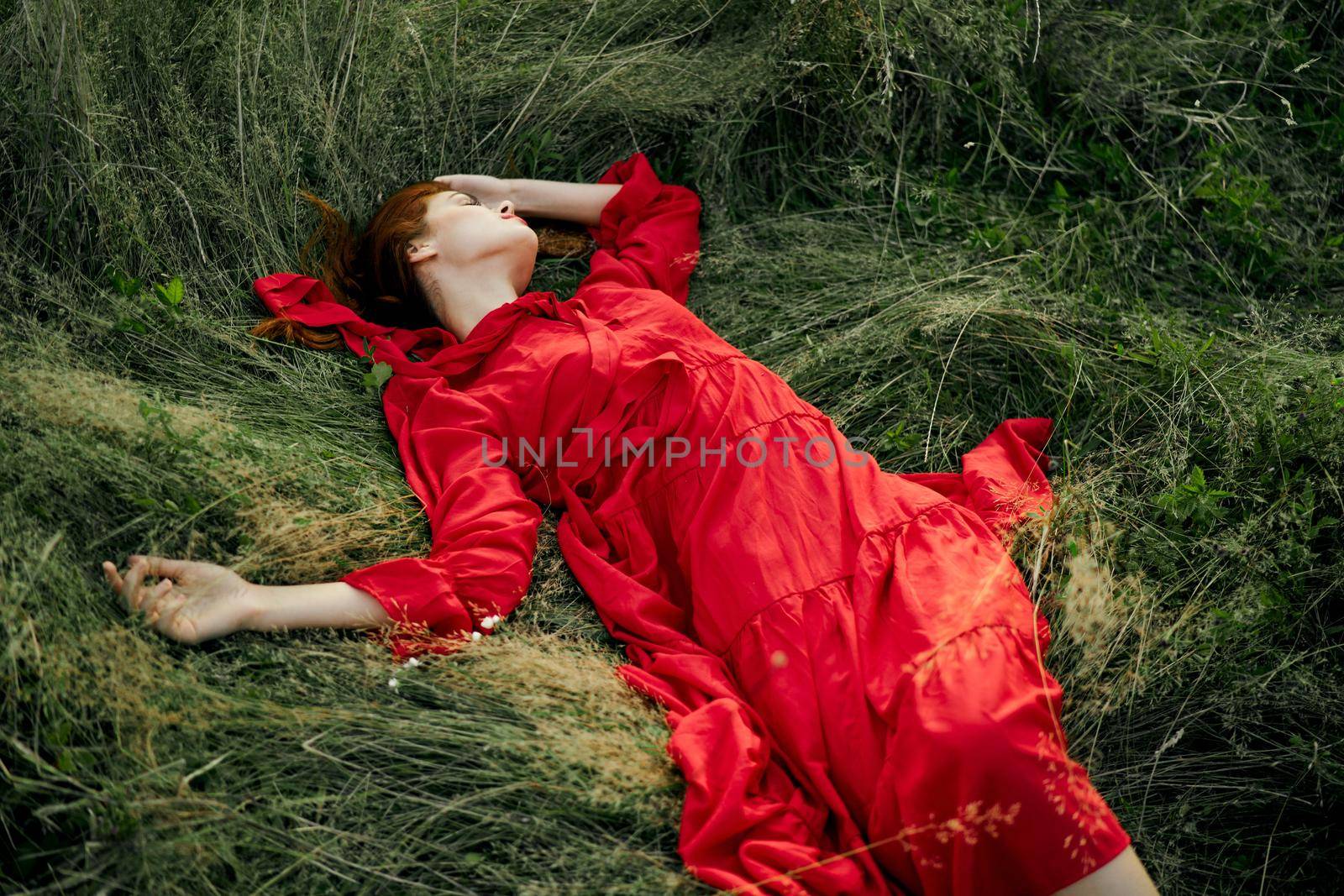 woman in red dress lies on the grass in the field nature landscape. High quality photo