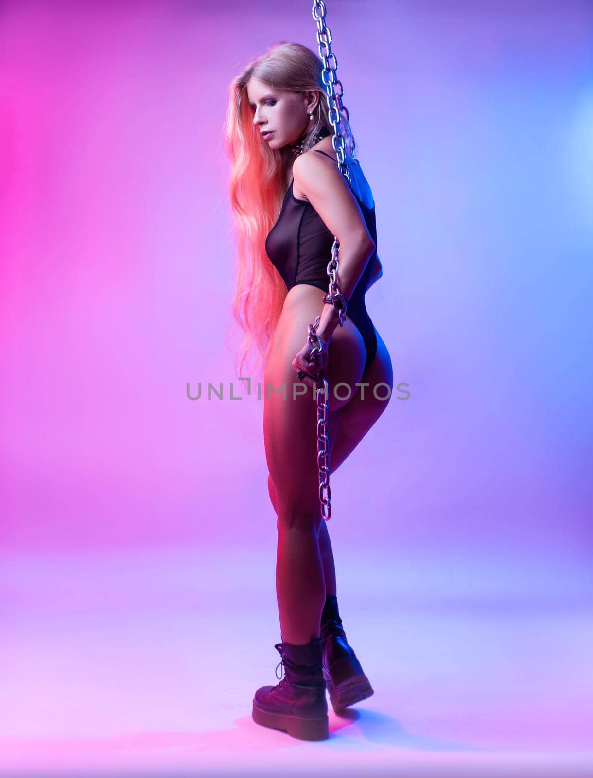 Sexy blonde girl with long hair stands in neon light with long chains by Rotozey