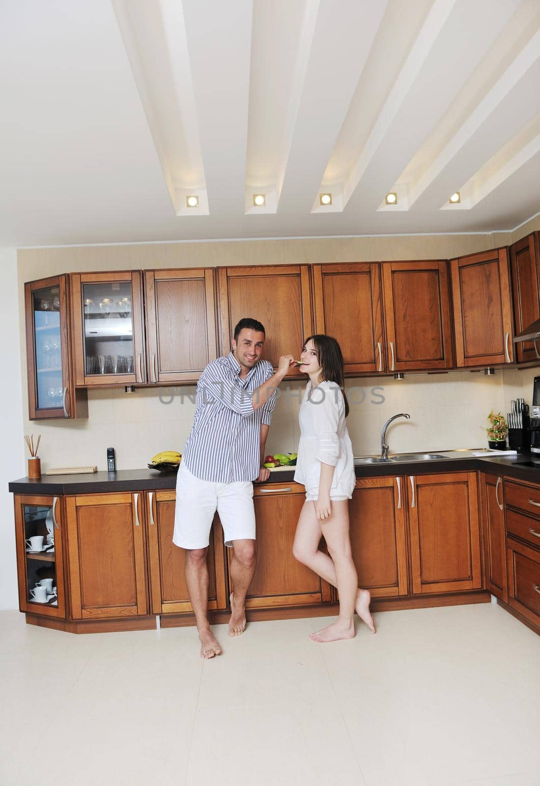 happy young couple have fun in modern wooden  kitchen indoor while preparing fresh food