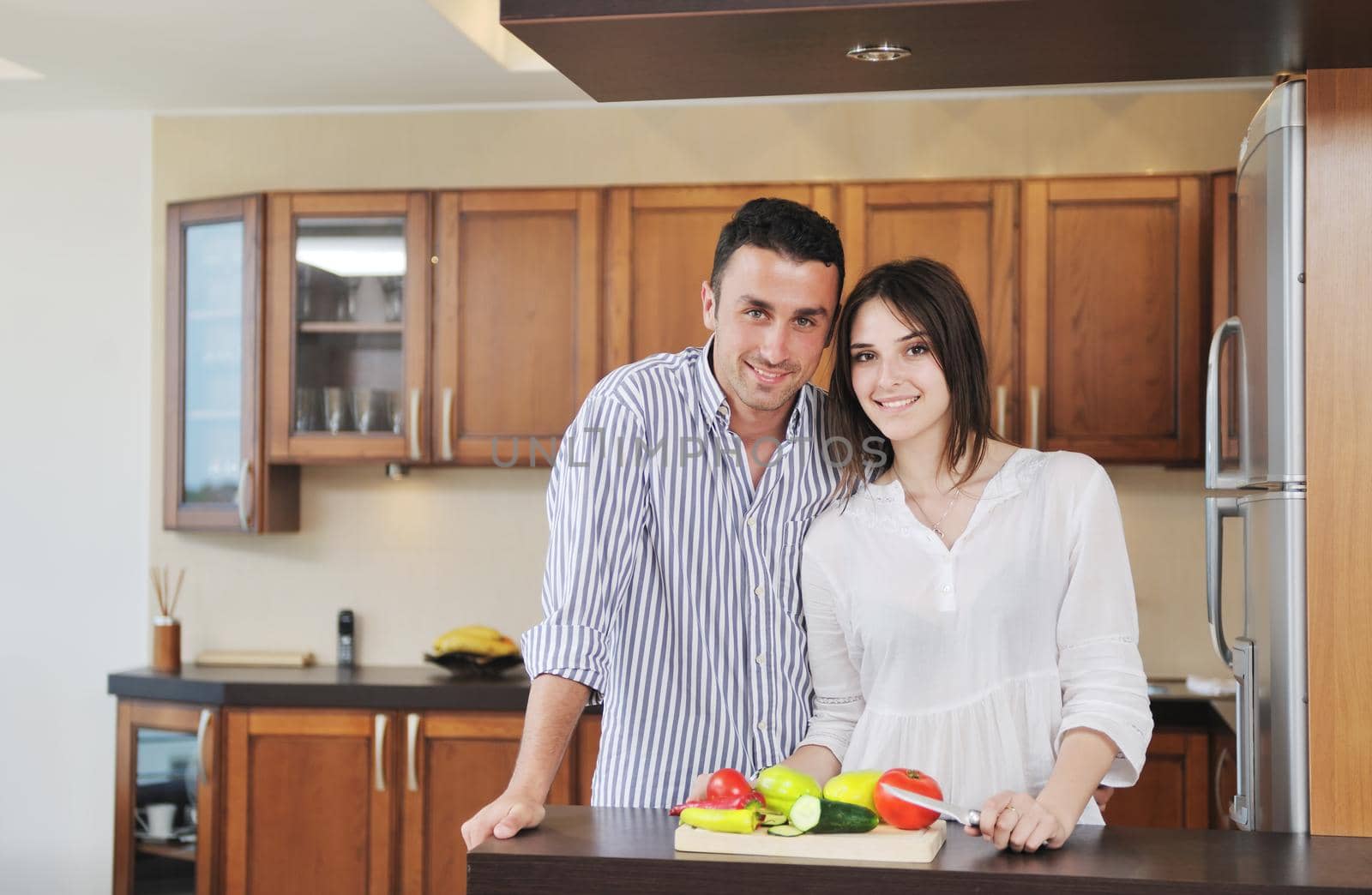 happy young couple have fun in modern wooden  kitchen indoor while preparing fresh food