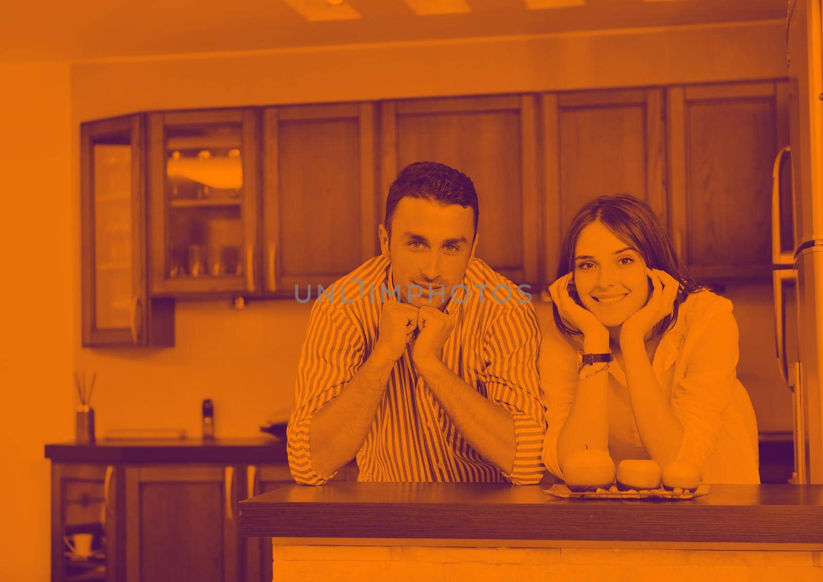 happy young couple have fun in modern wooden  kitchen indoor while preparing fresh food duo tone