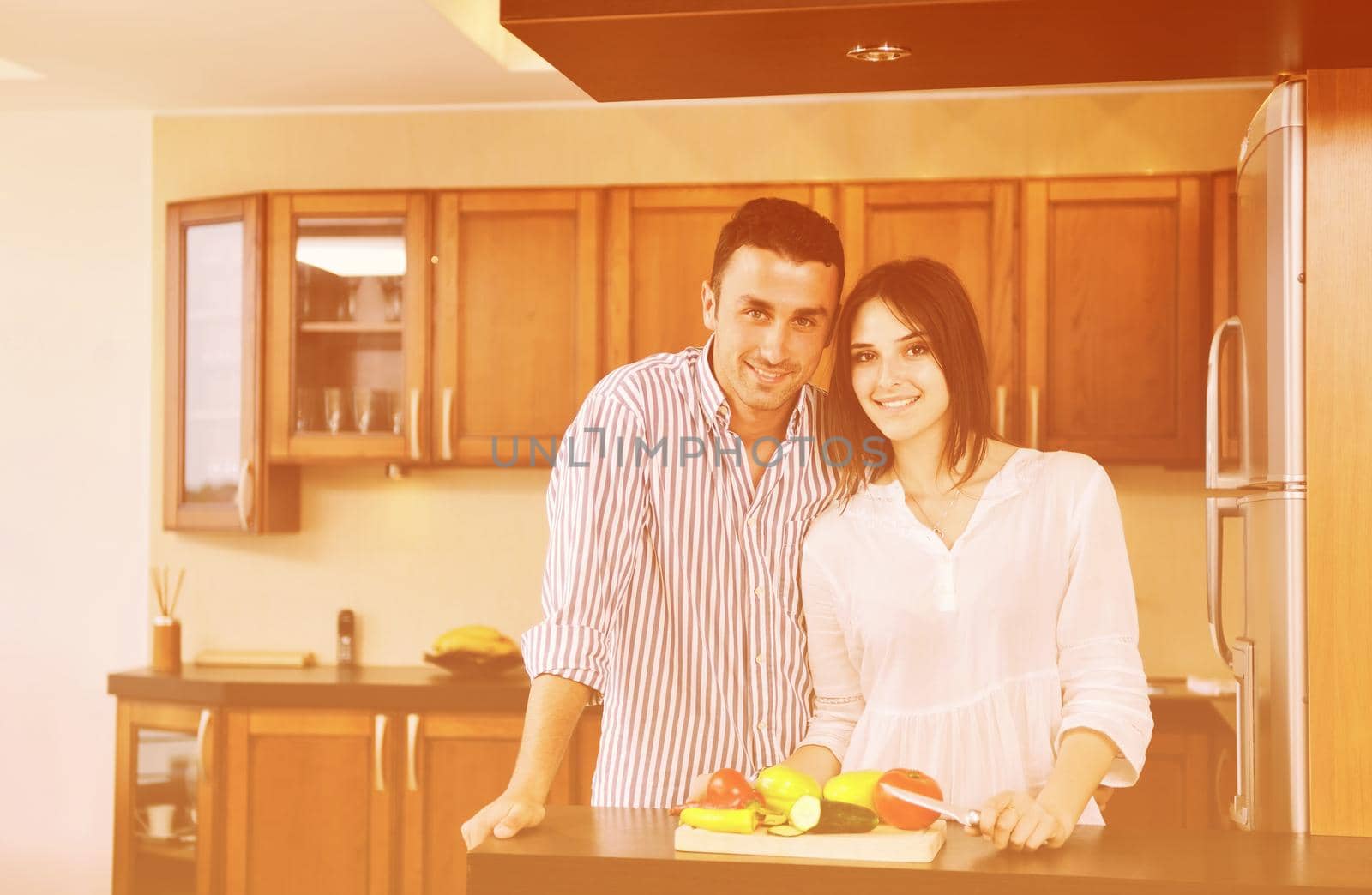 happy young couple have fun in modern wooden  kitchen indoor while preparing fresh food