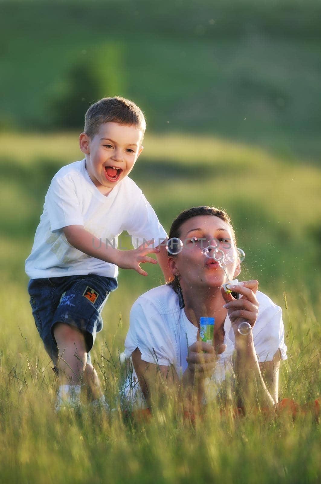 happy child and woman outdoor playing with soap bubble on meadow