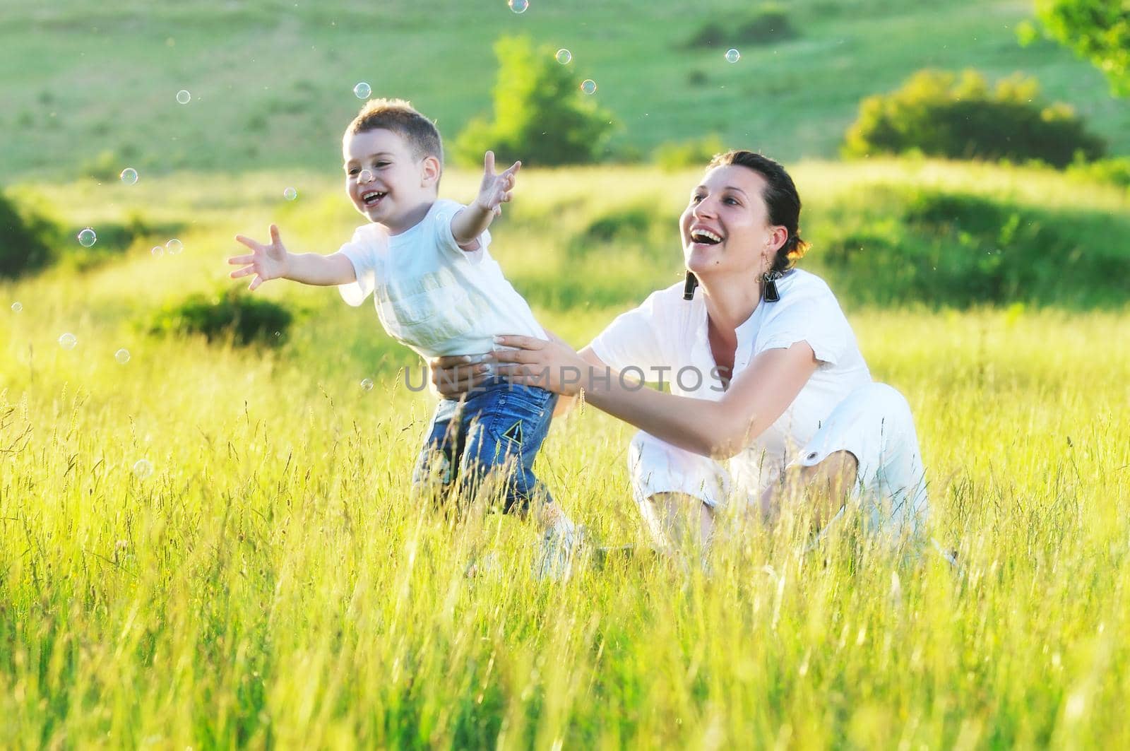 happy child and woman outdoor playing with soap bubble on meadow