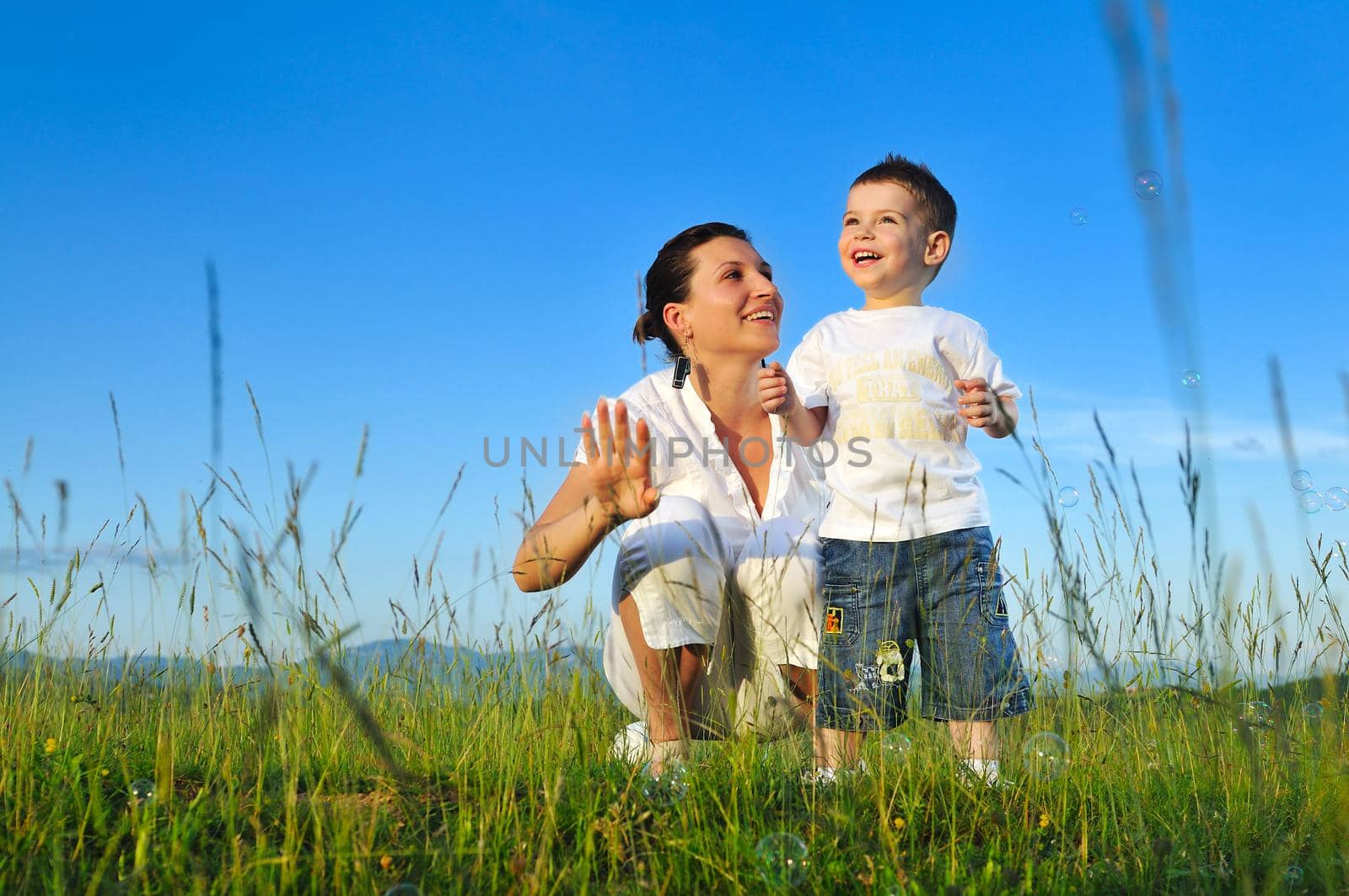 happy child and woman outdoor playing with soap bubble on meadow