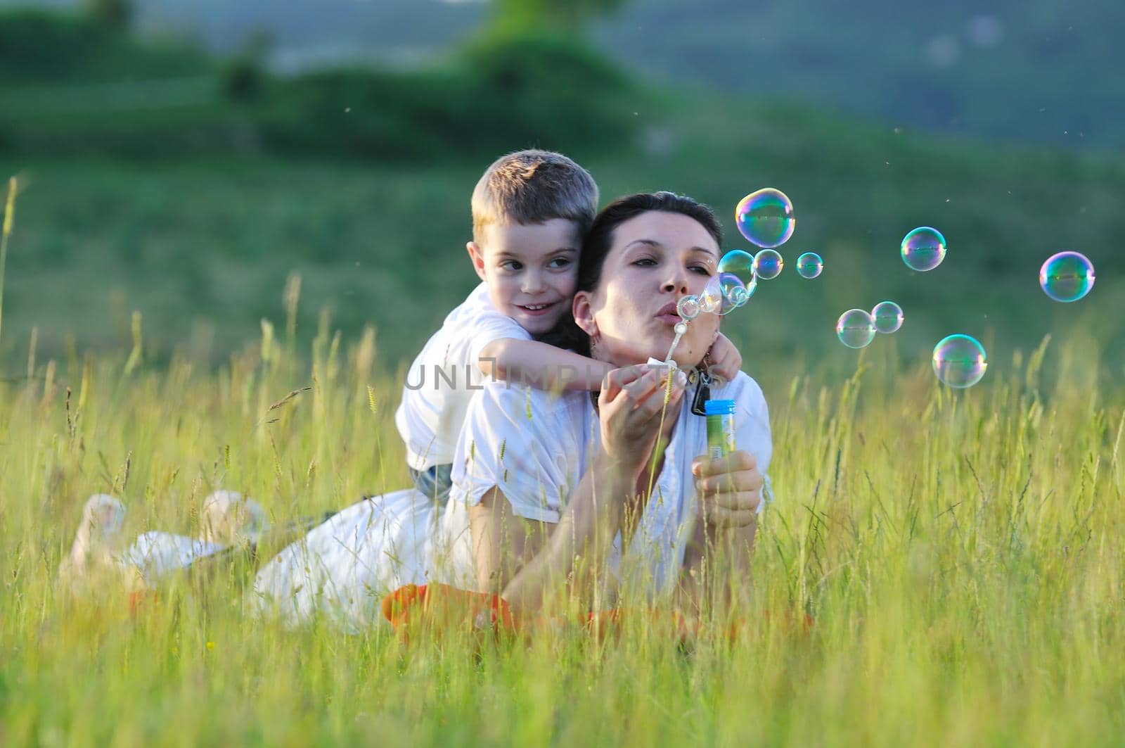 happy child and woman outdoor playing with soap bubble on meadow